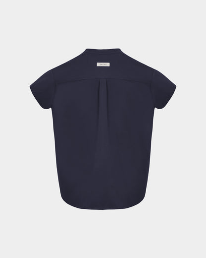 A navy short-sleeve scrub shirt shown from the back, featuring a subtle center back pleat and a small rectangular brand label at the collar, set against a light gray background.