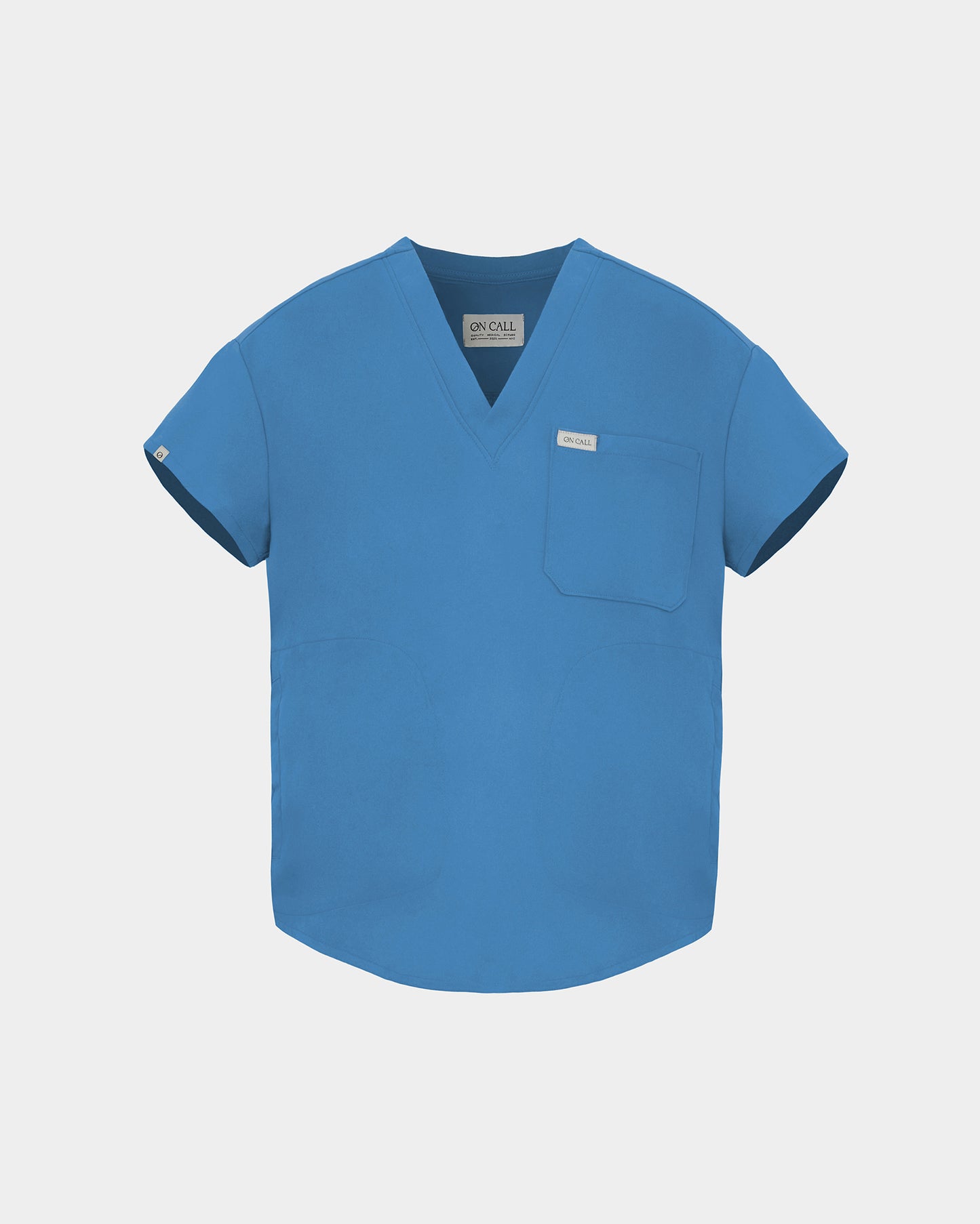 A bright blue V-neck scrub top with short sleeves, a chest pocket, and a small white brand tag, shown on a light gray background.