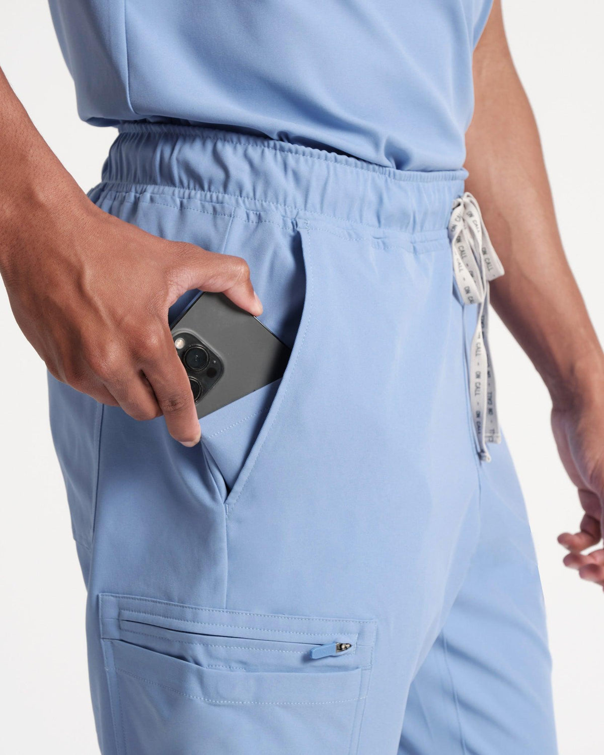 Close up man in light blue cargo scrub pants with hand pulling out a cell phone of the waist pocket.