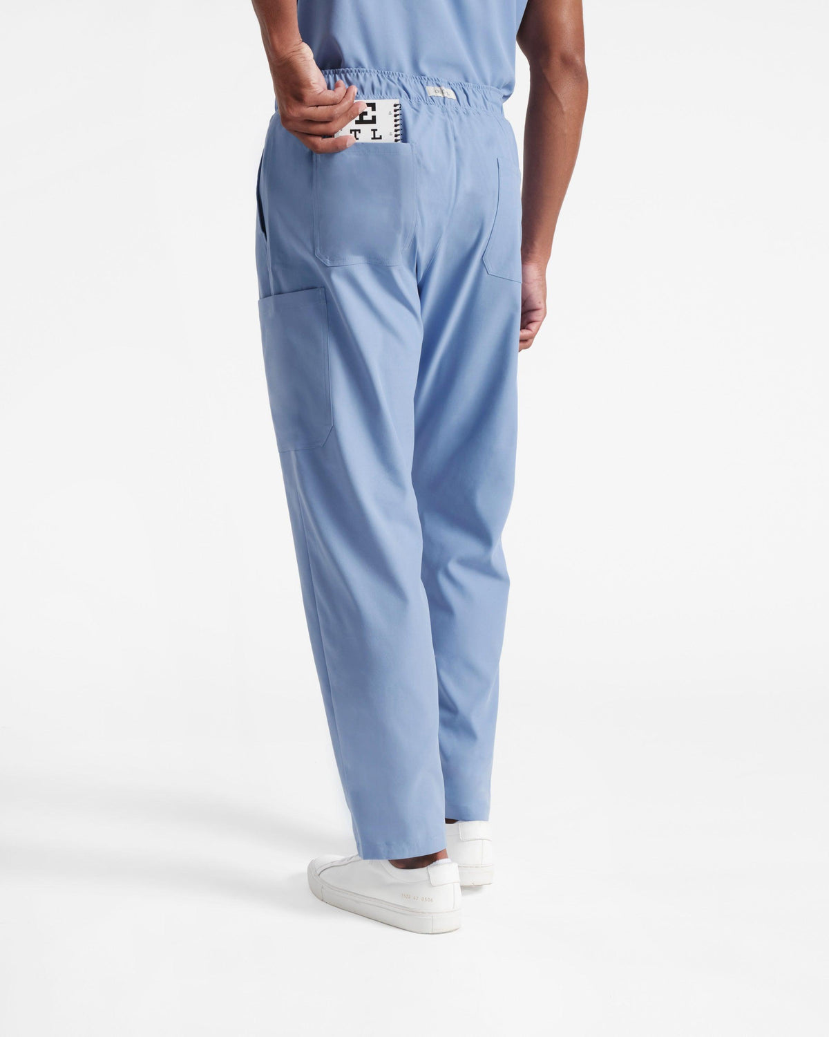 Back side view of man in light blue cargo scrub pants pulling a pocket eye chart out of the left back pocket.