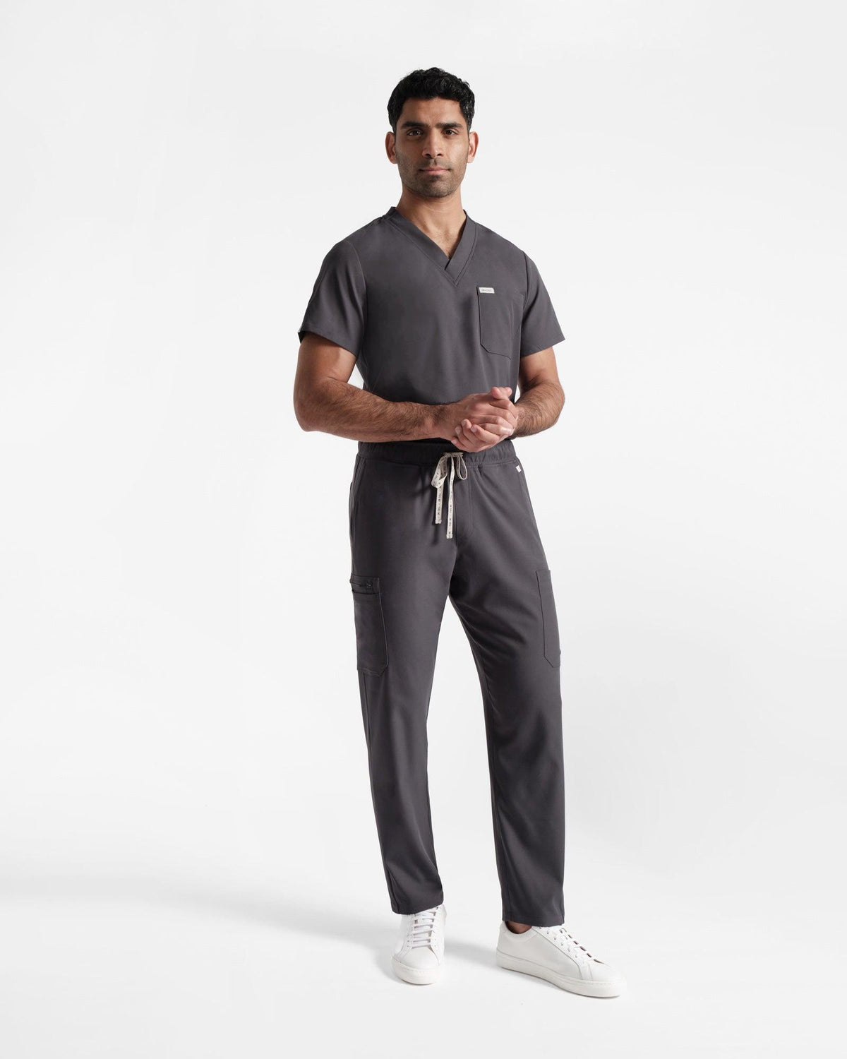 Man in dark grey cargo scrub pants with a matching v-neck scrub shirt tucked in. 