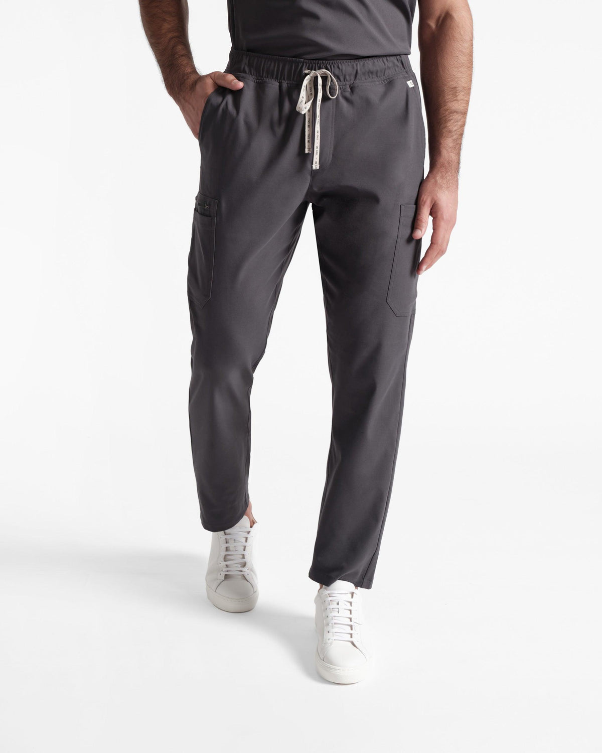 Model from the waist down in men's dark grey cargo scrub pants with hand in waist pocket.