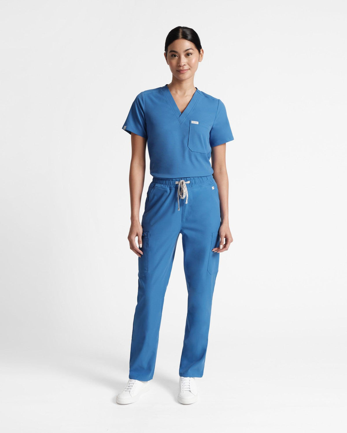 Woman in a bright blue scrub v-neck scrub shirt tucked into matching cargo straight leg scrub pants. 