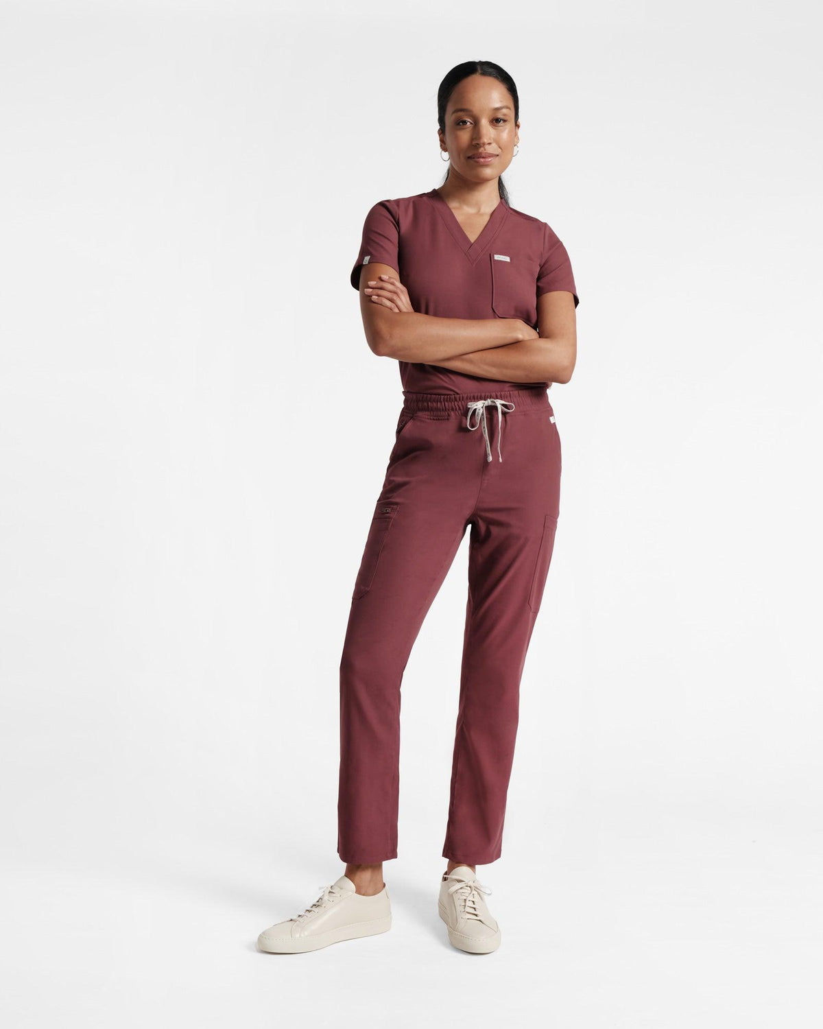 Woman in a deep red v-neck scrub shirt tucked into matching cargo straight leg scrub pants.