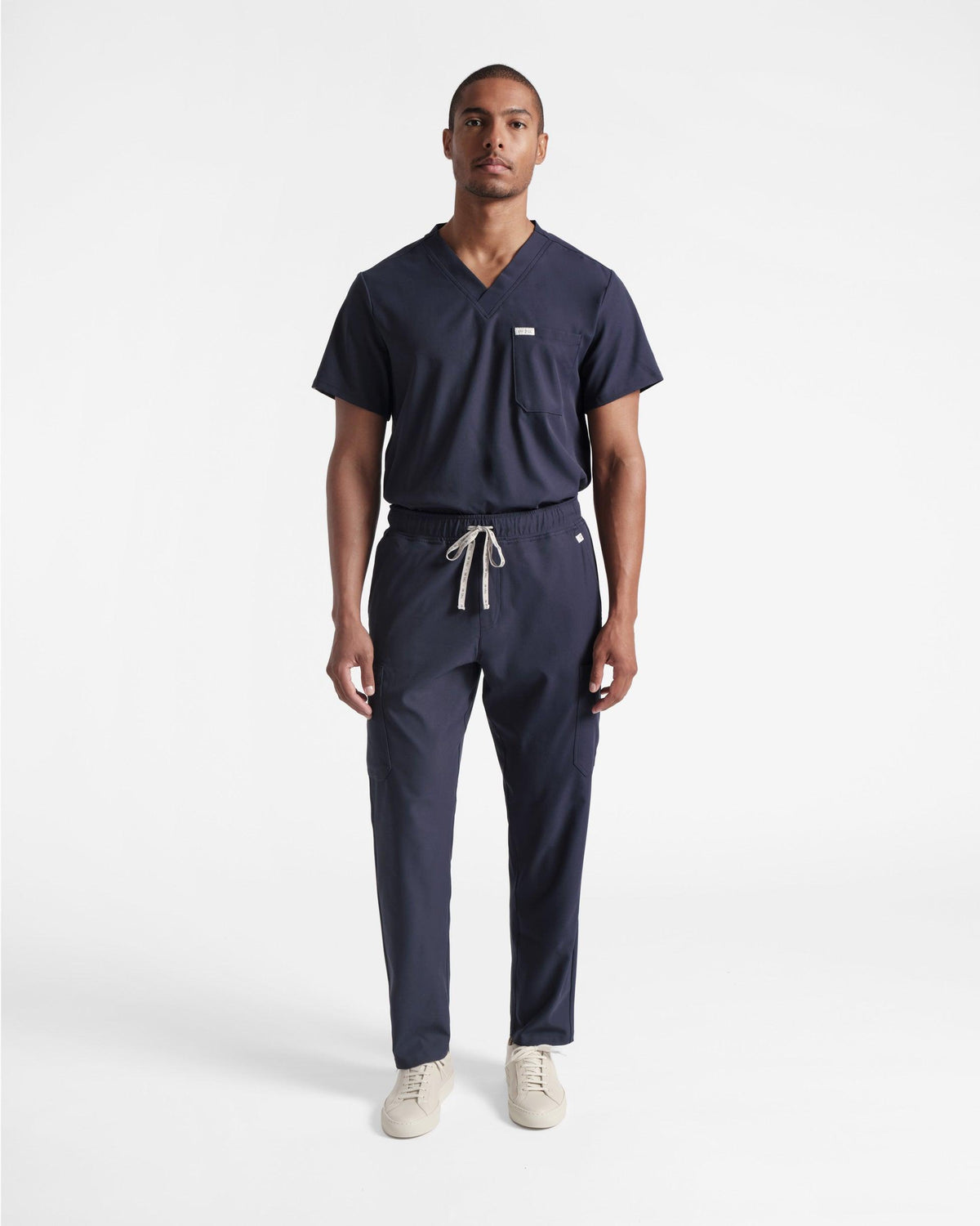 Man in navy cargo scrub pants with a matching v-neck scrub shirt tucked in.