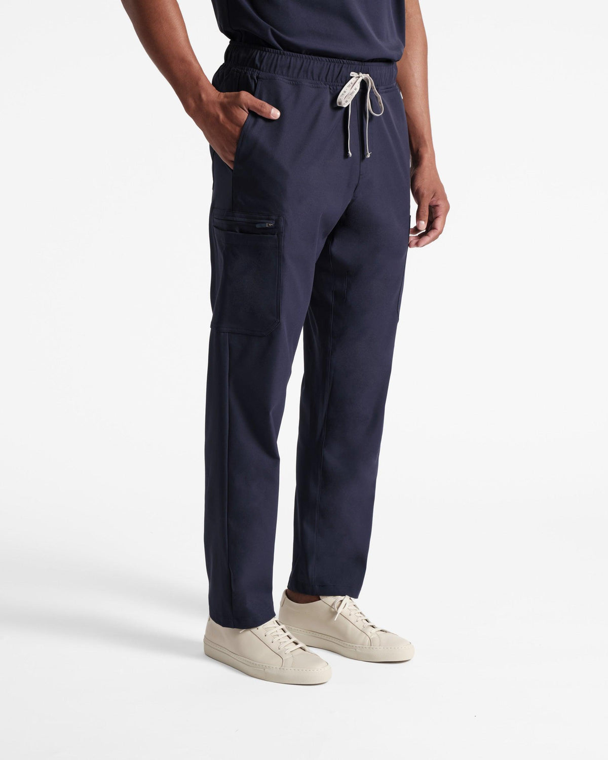 Angled front view of man in navy cargo scrub pants with hand inside of waist pocket. 