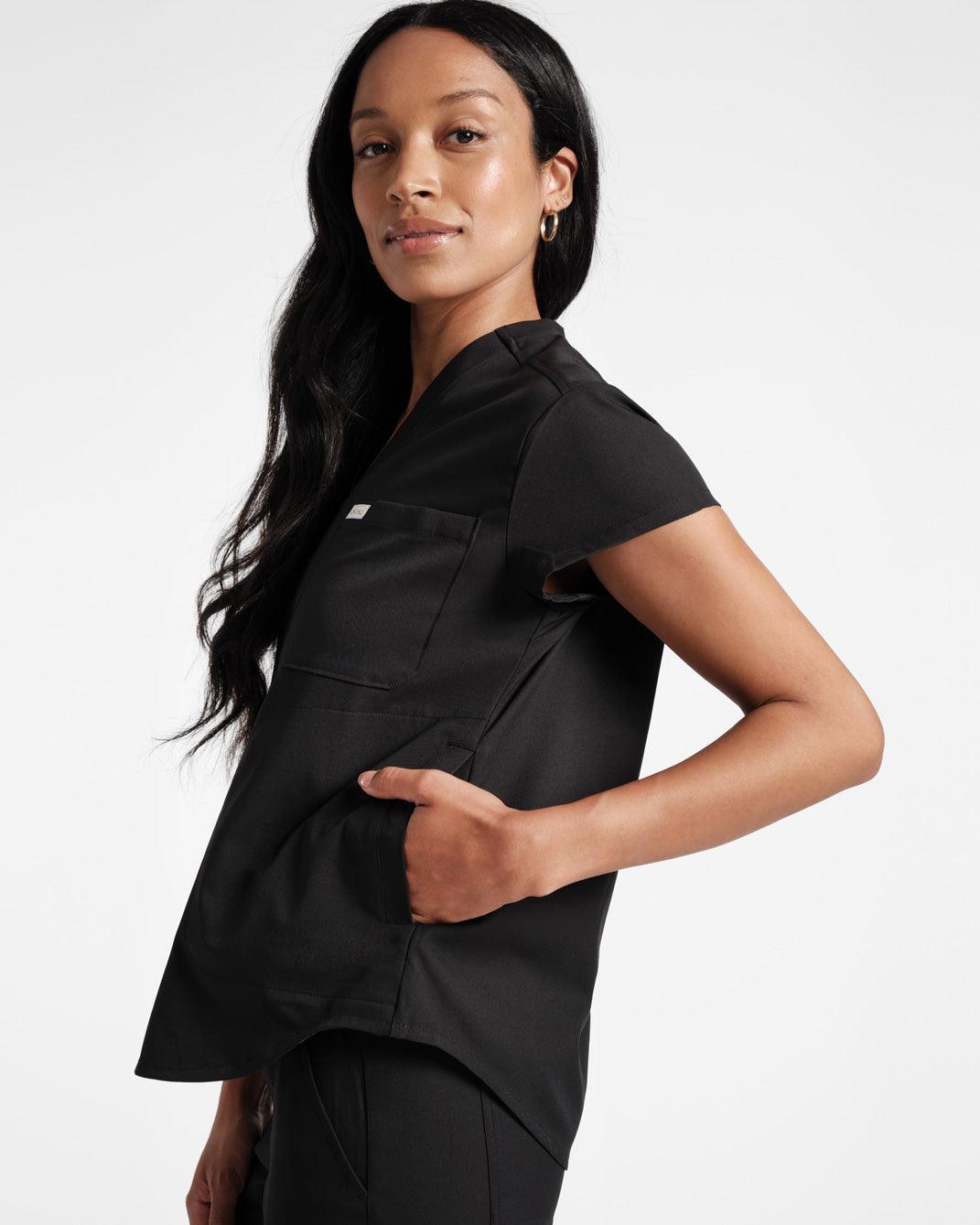 Side view of woman wearing black scrub top with chest pocket and hand in side pocket.