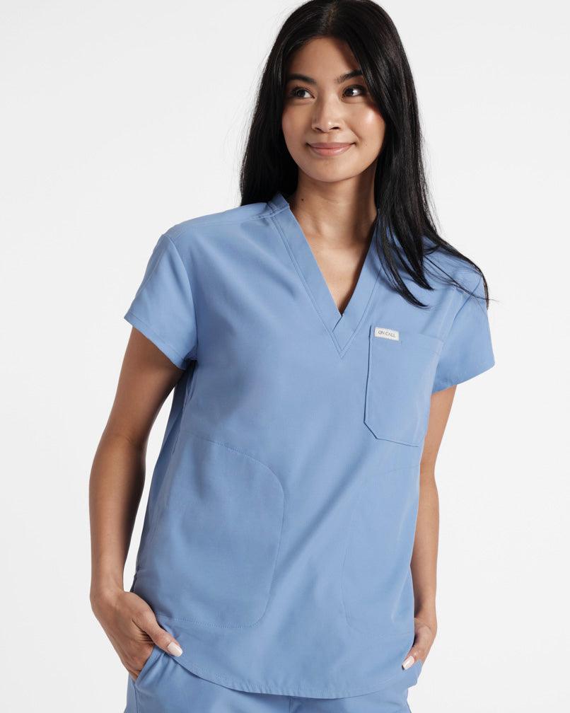 Woman in v-neck light blue scrub shirt with chest pocket and two side pockets.