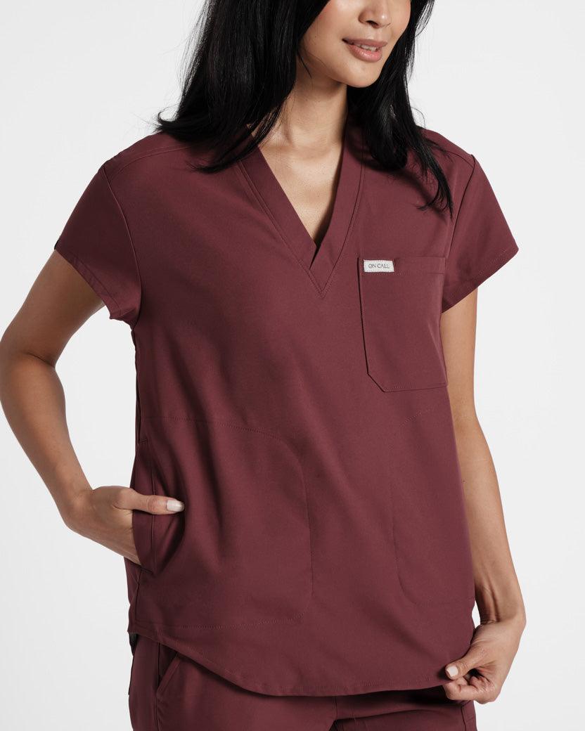 Close up view of woman wearing deep red v-neck scrub shirt with her hand in one of the side pockets.
