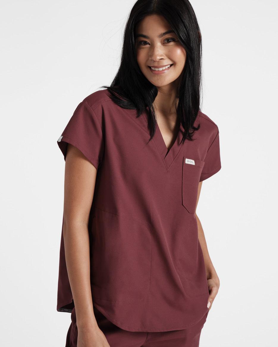 Woman wearing a deep red v-neck scrub shirt with a chest pocket.
