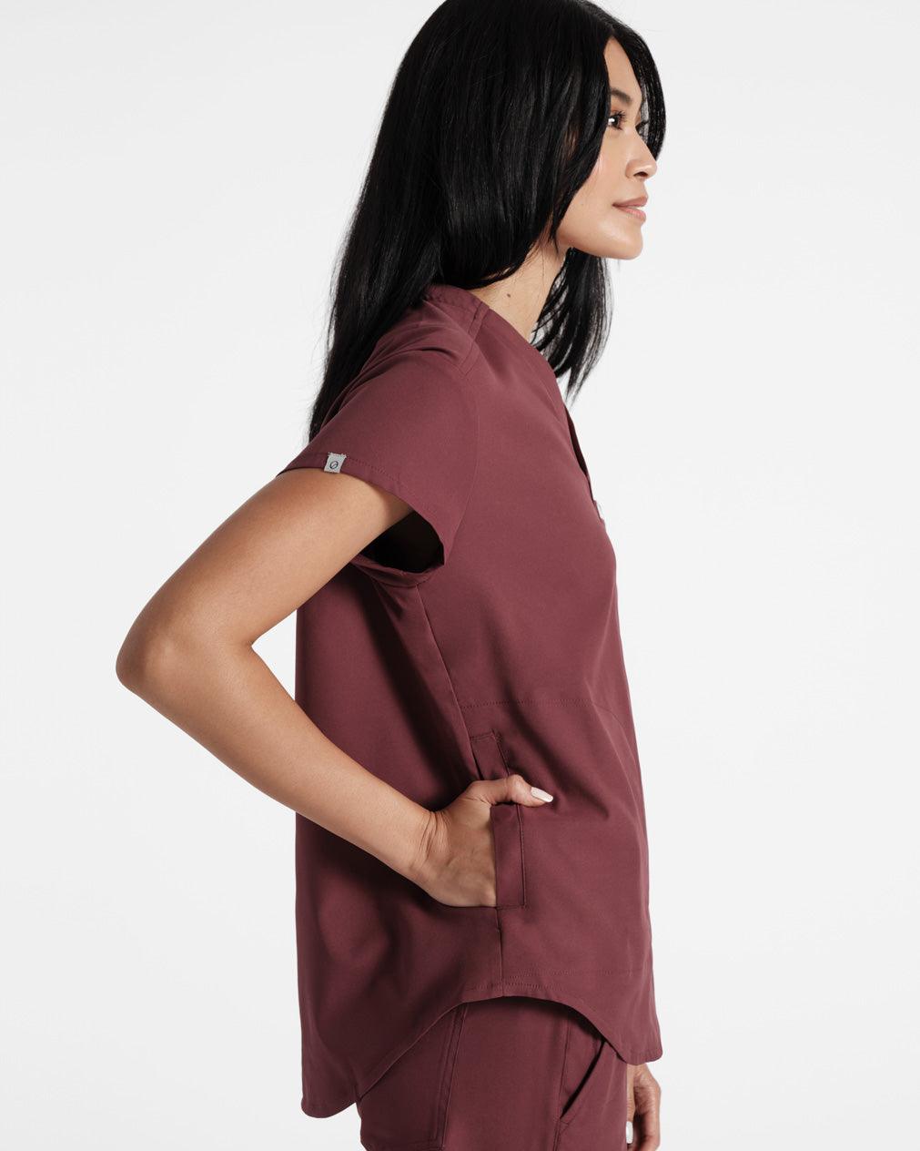 Side view of woman in deep red scrubs with her hand in the shirt pocket and a small fabric logo label folded over the sleeve hem.