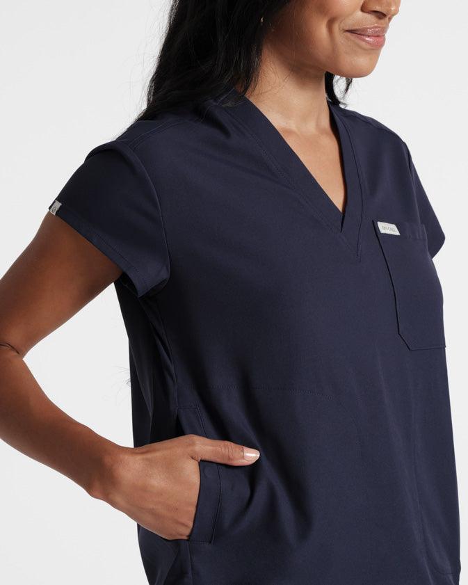 Close up angled view of woman in navy v-neck scrub shirt with chest pocket and hand in one of the side pockets.