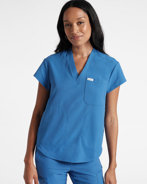 A woman wearing a v-neck, bright blue scrub top with a spacious chest pocket and a side pockets.
