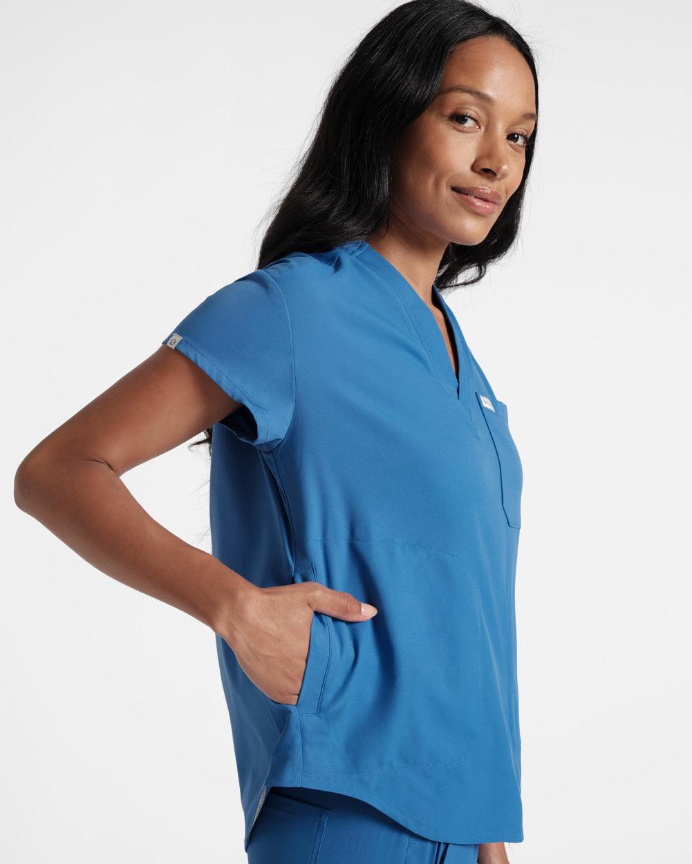 Side view of woman with her hand ini the pocket of a v-neck bright blue scrub shirt.
