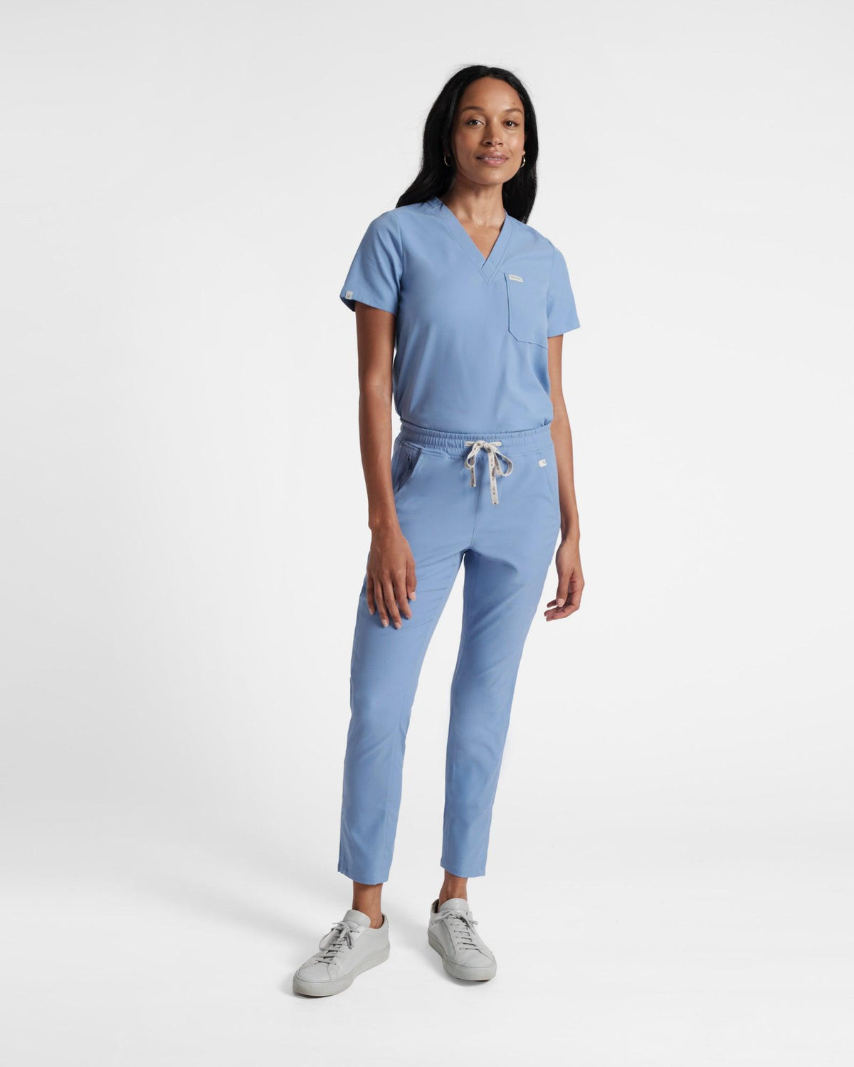 Woman in full matching light blue scrubs with a v-neck shirt and straight leg pants.