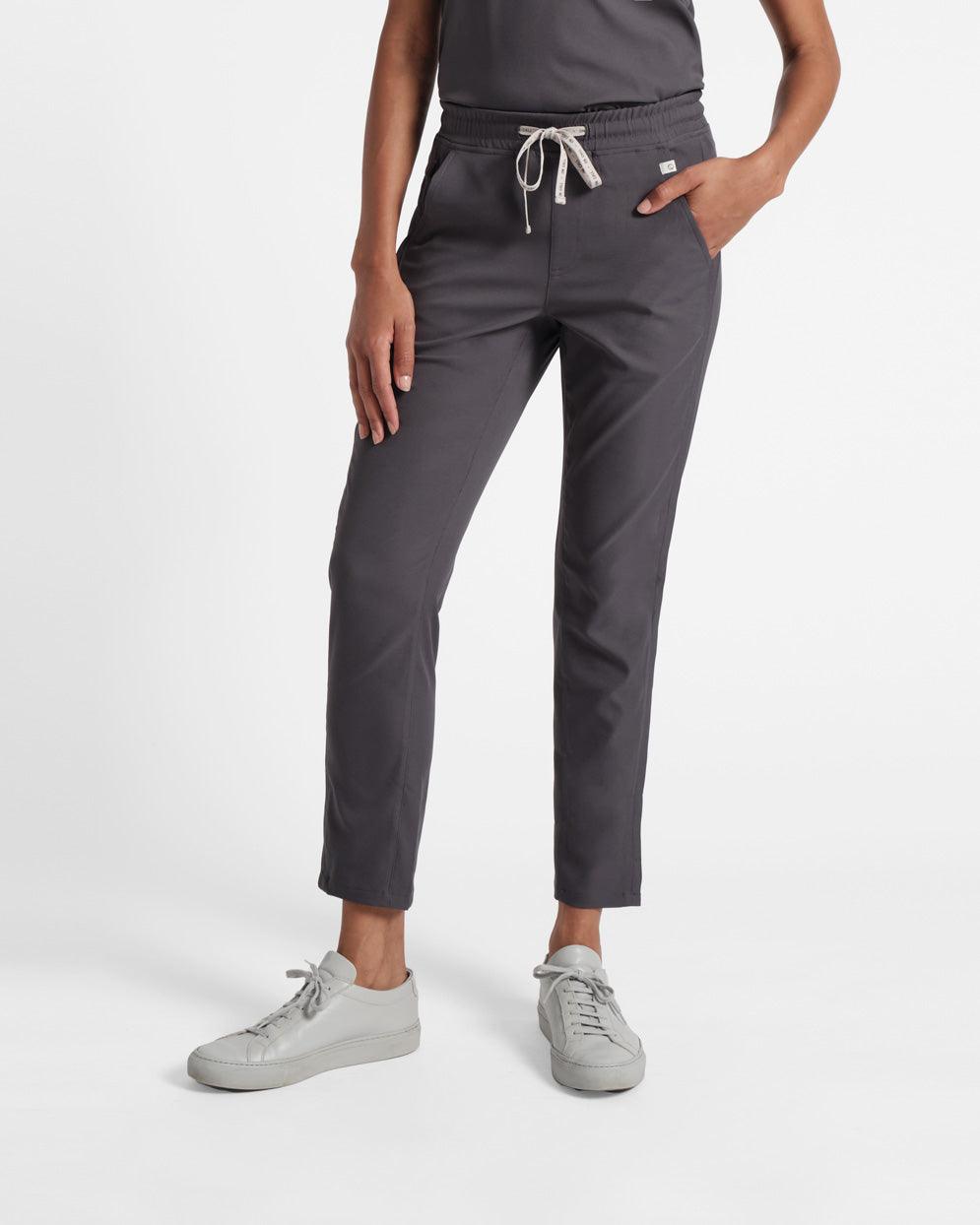 Waist down shot of woman in dark grey straight leg scrub pants with hand in pocket.