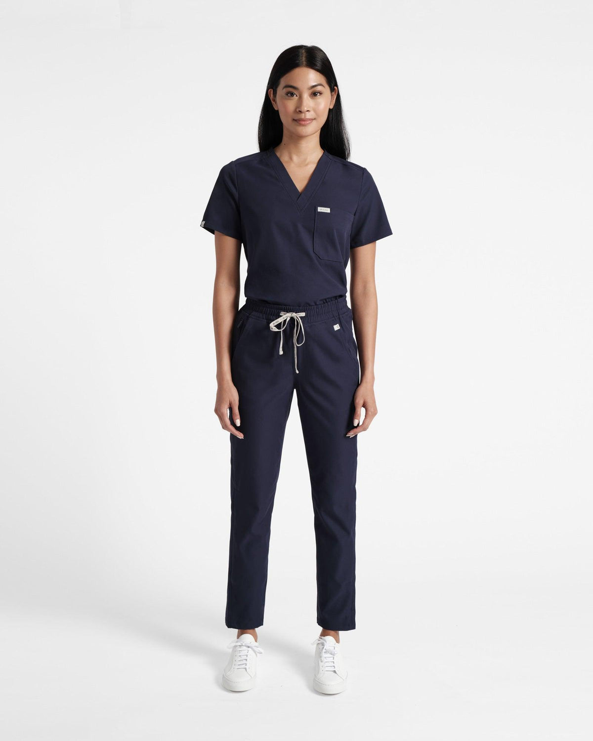 Woman wearing a matching navy scrub set of a v-neck shirt and straight leg pants.