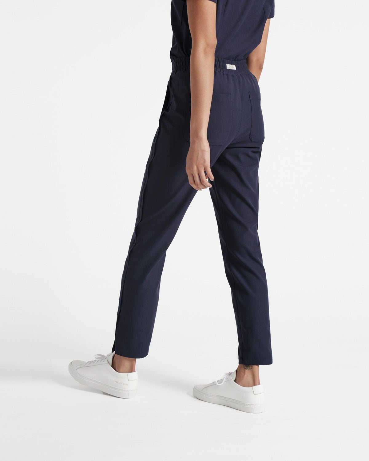 Angled back view of woman in navy straight leg scrub pants with small ankle slit.