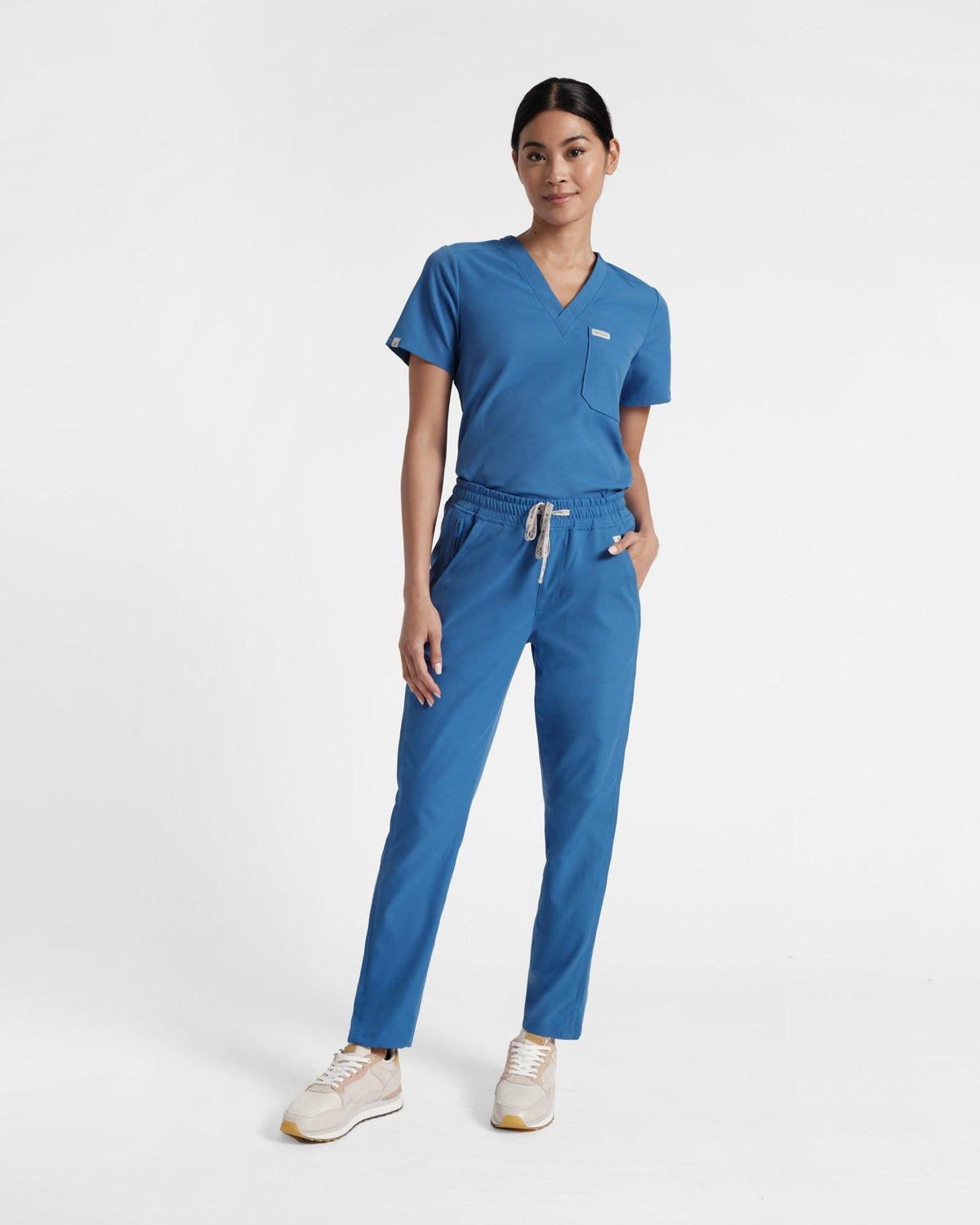 Woman in bright blue matching scrubs with a v-neck top and straight leg pants.