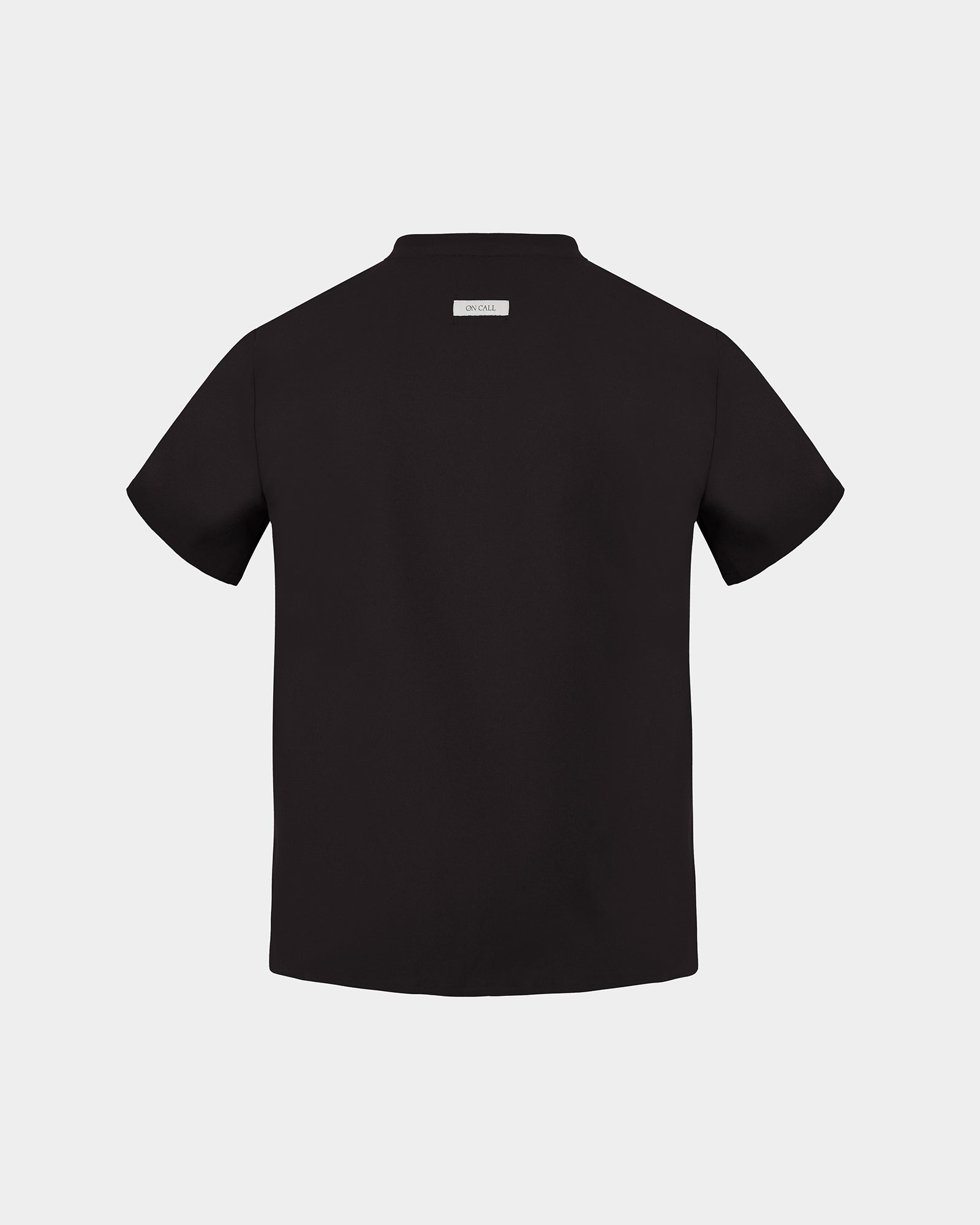 A black short-sleeve scrub shirt shown from the back, featuring a small rectangular brand label at the collar, set against a solid light gray background.