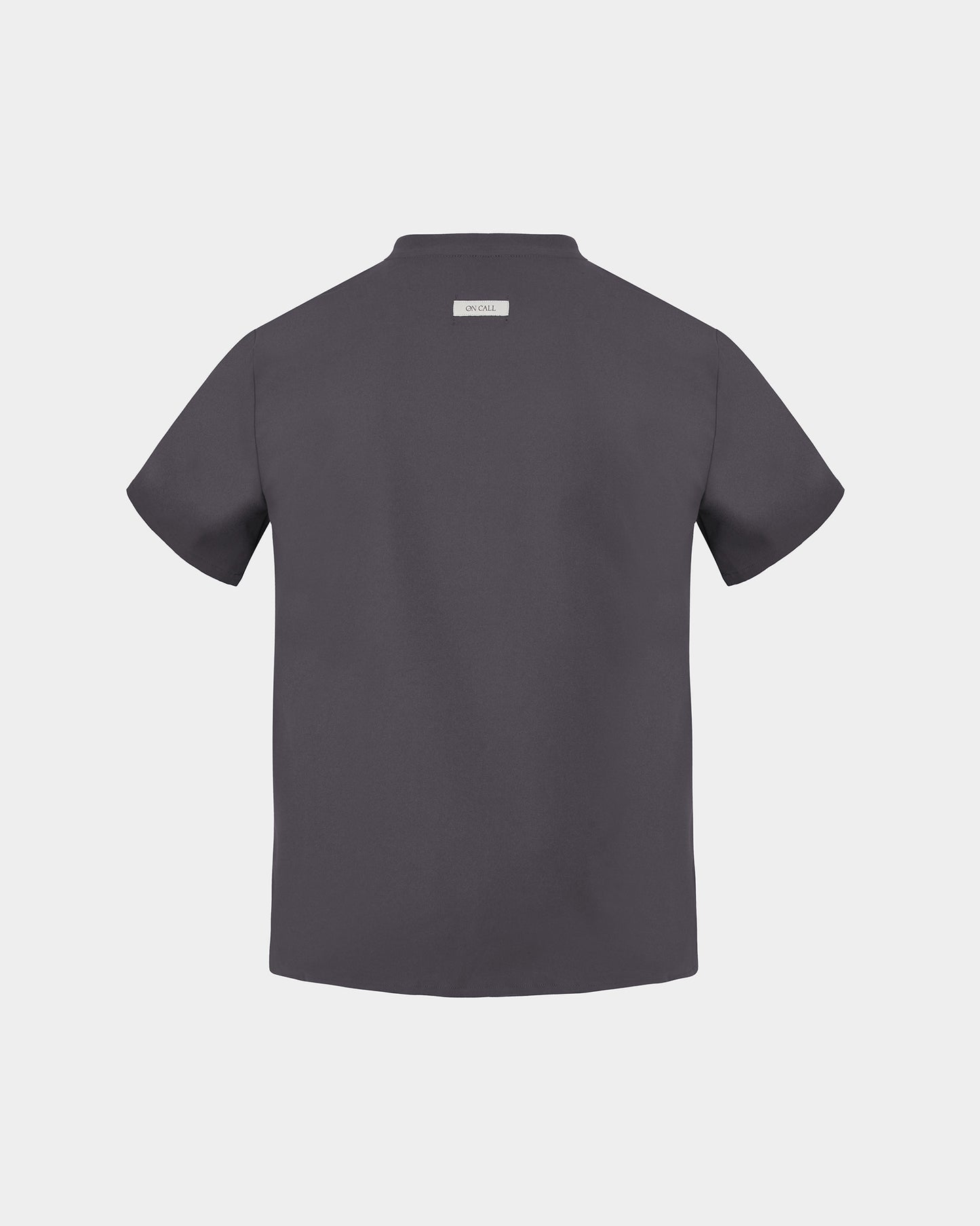 A black short-sleeve scrub shirt shown from the back, featuring a small rectangular brand label at the collar, set against a solid light gray background.