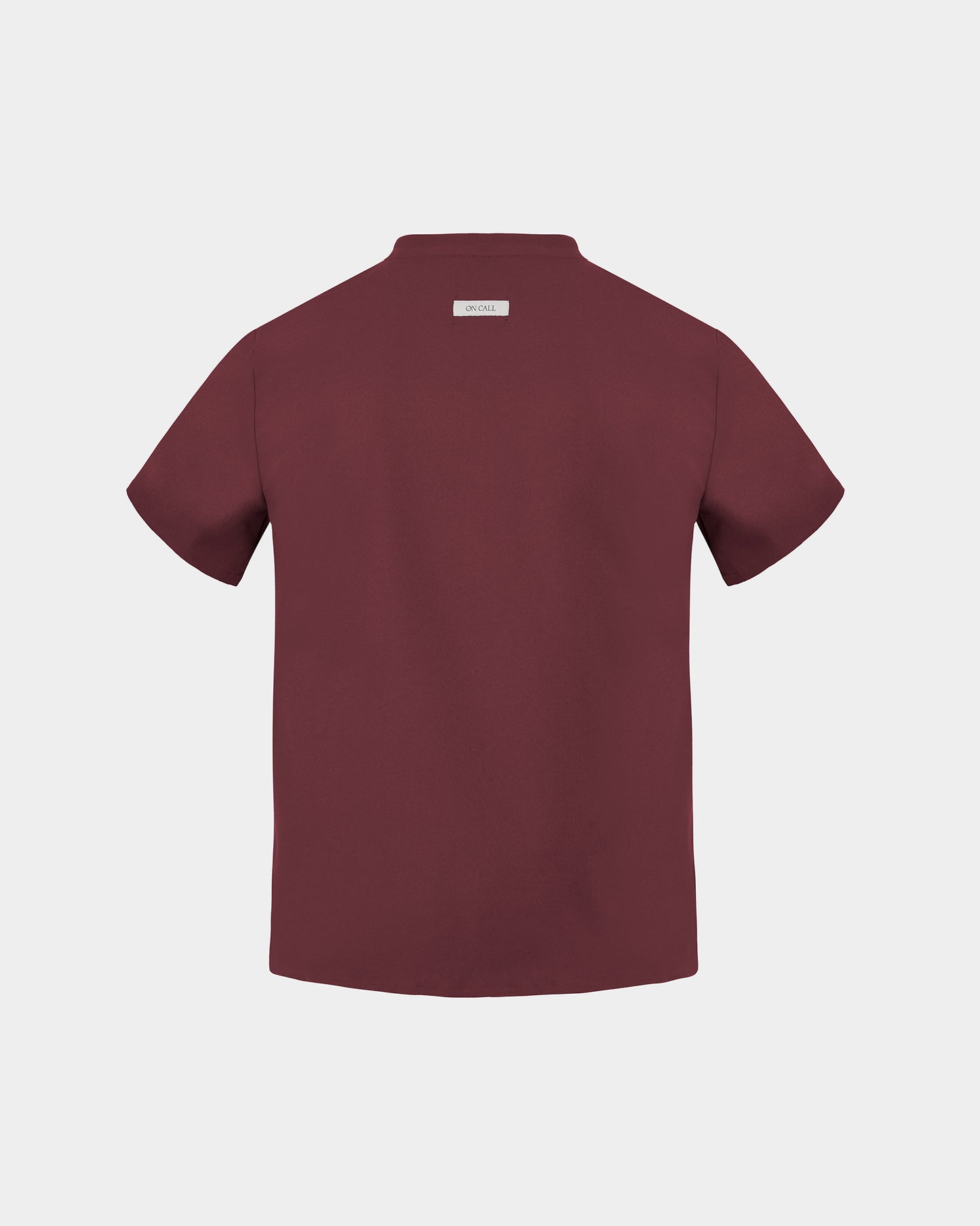 A heme red short-sleeve scrub shirt shown from the back, featuring a small rectangular brand label at the collar, set against a solid light gray background.
