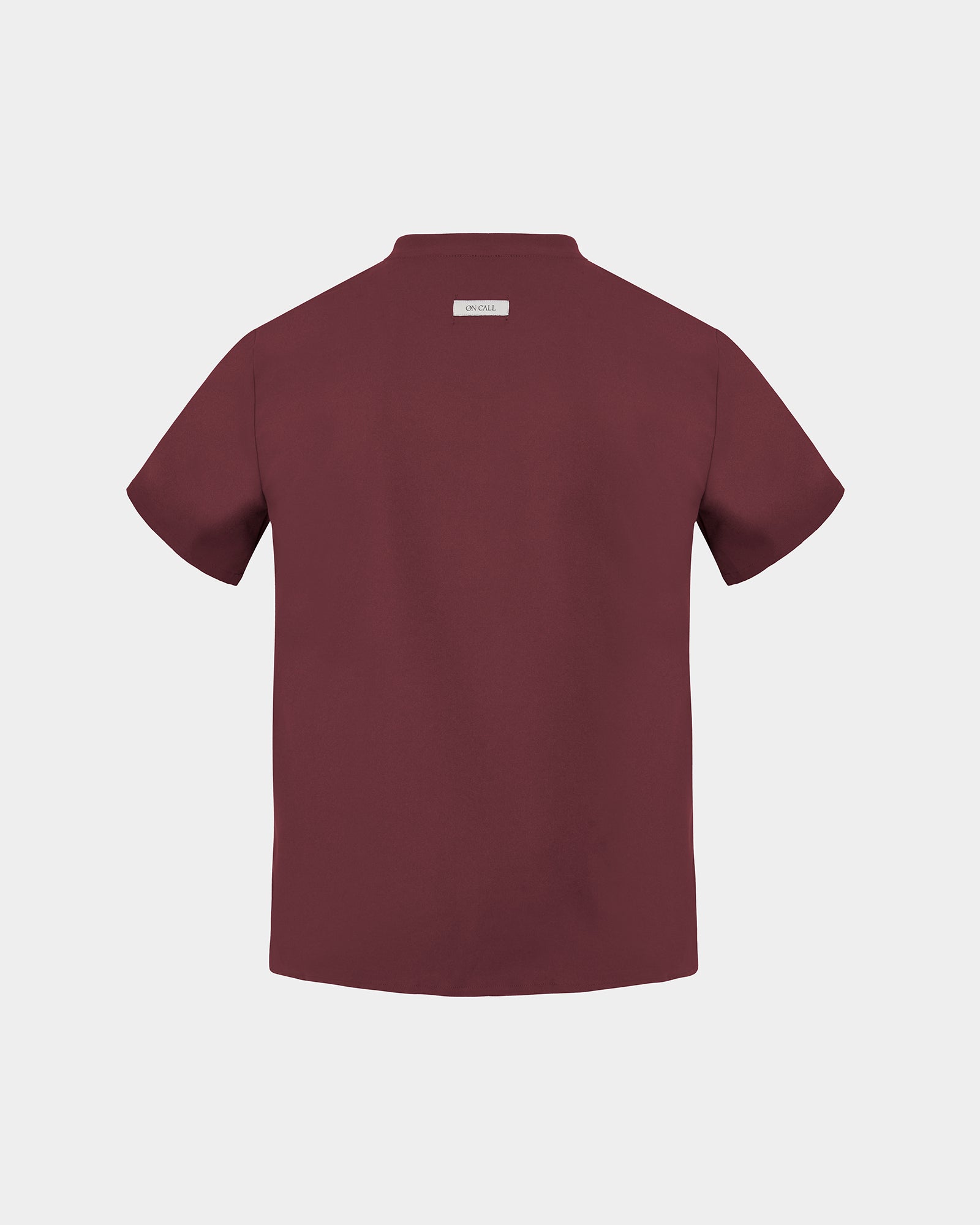 A heme red short-sleeve scrub shirt shown from the back, featuring a small rectangular brand label at the collar, set against a solid light gray background.