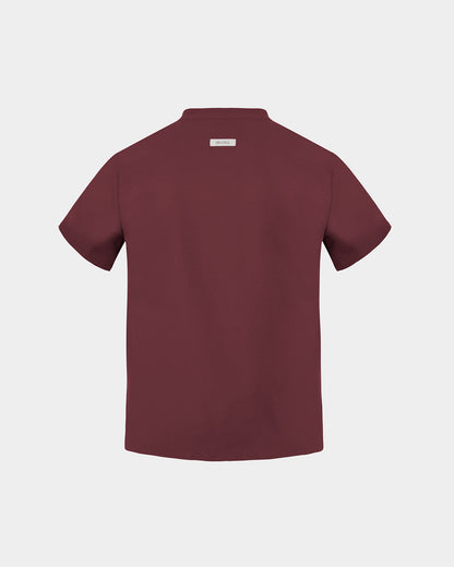 A heme red short-sleeve scrub shirt shown from the back, featuring a small rectangular brand label at the collar, set against a solid light gray background.