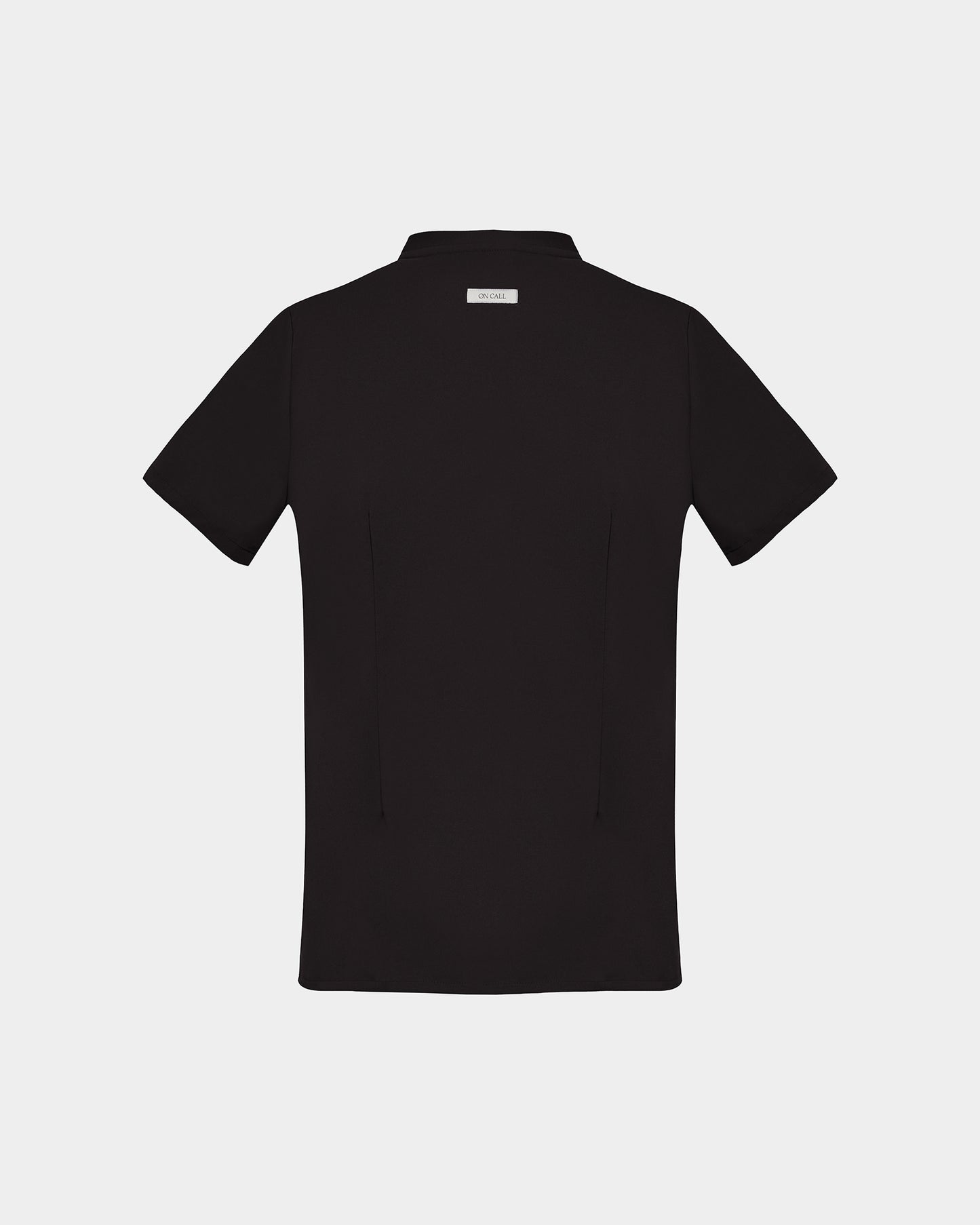 A back side view of a black short-sleeve scrub shirt with a logo label under the collar shown flat against a light gray background.