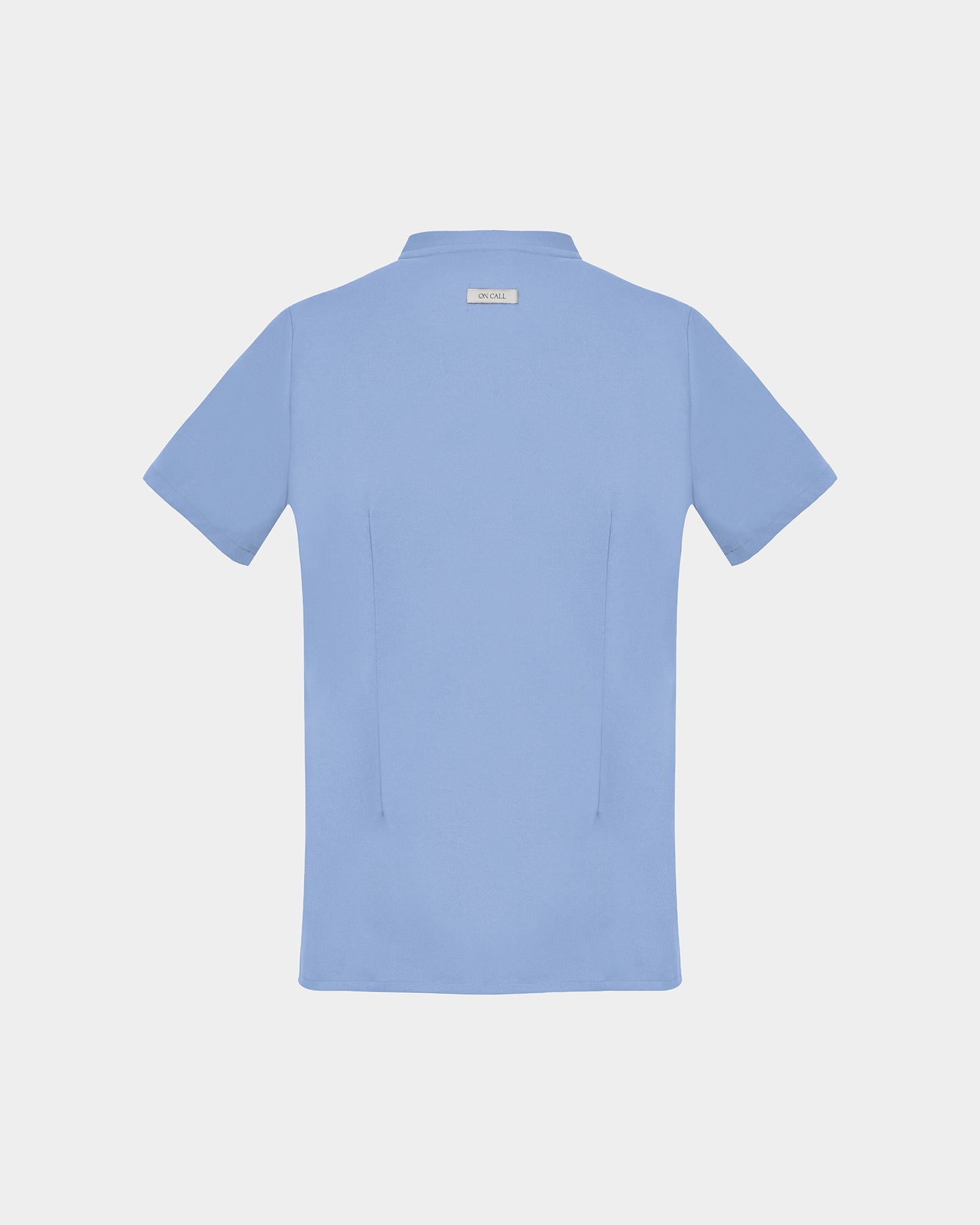 A light blue short-sleeve scrub shirt shown from the back, featuring two back darts, centered on a light gray background.