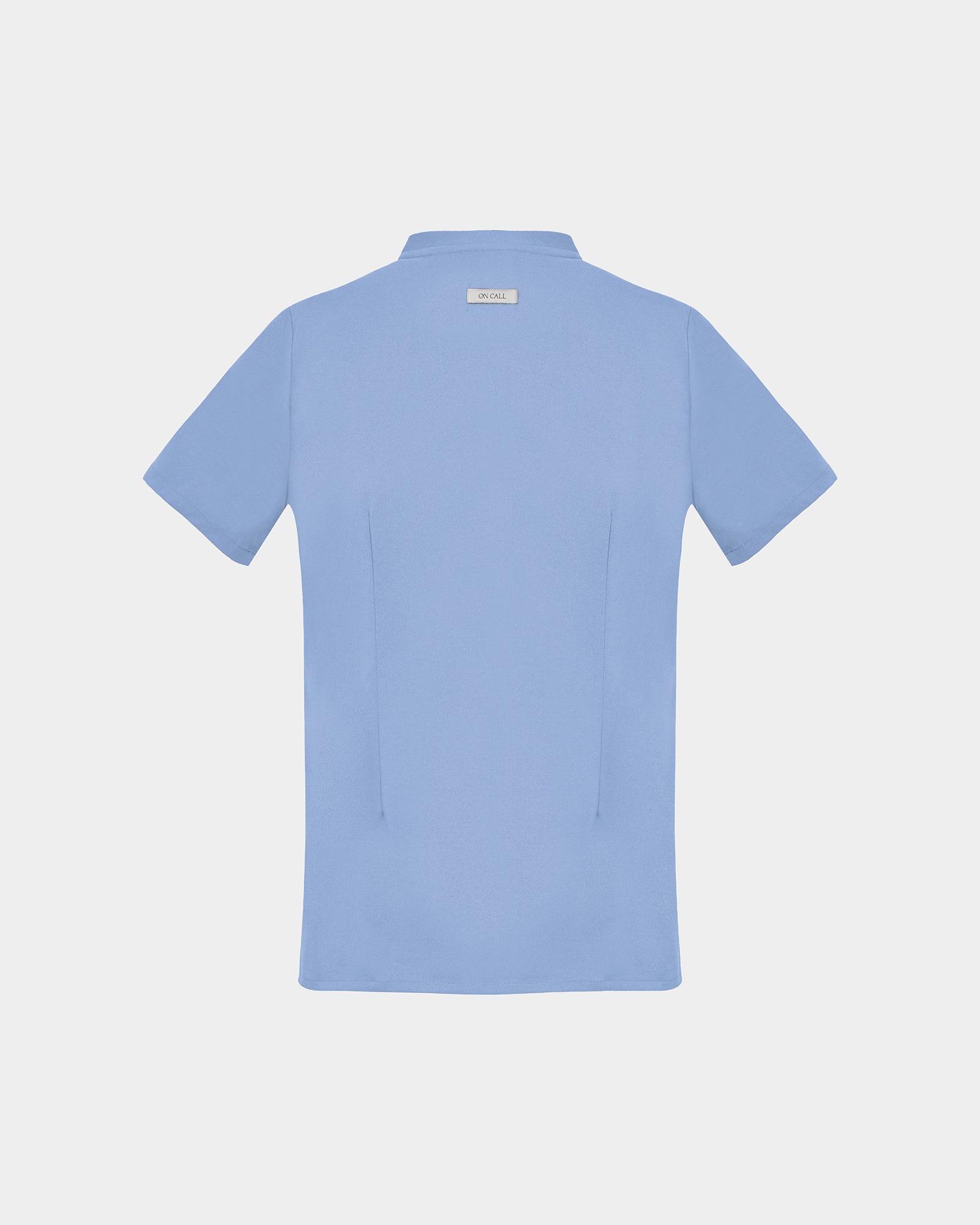 A light blue short-sleeve scrub shirt shown from the back, featuring two back darts, centered on a light gray background.