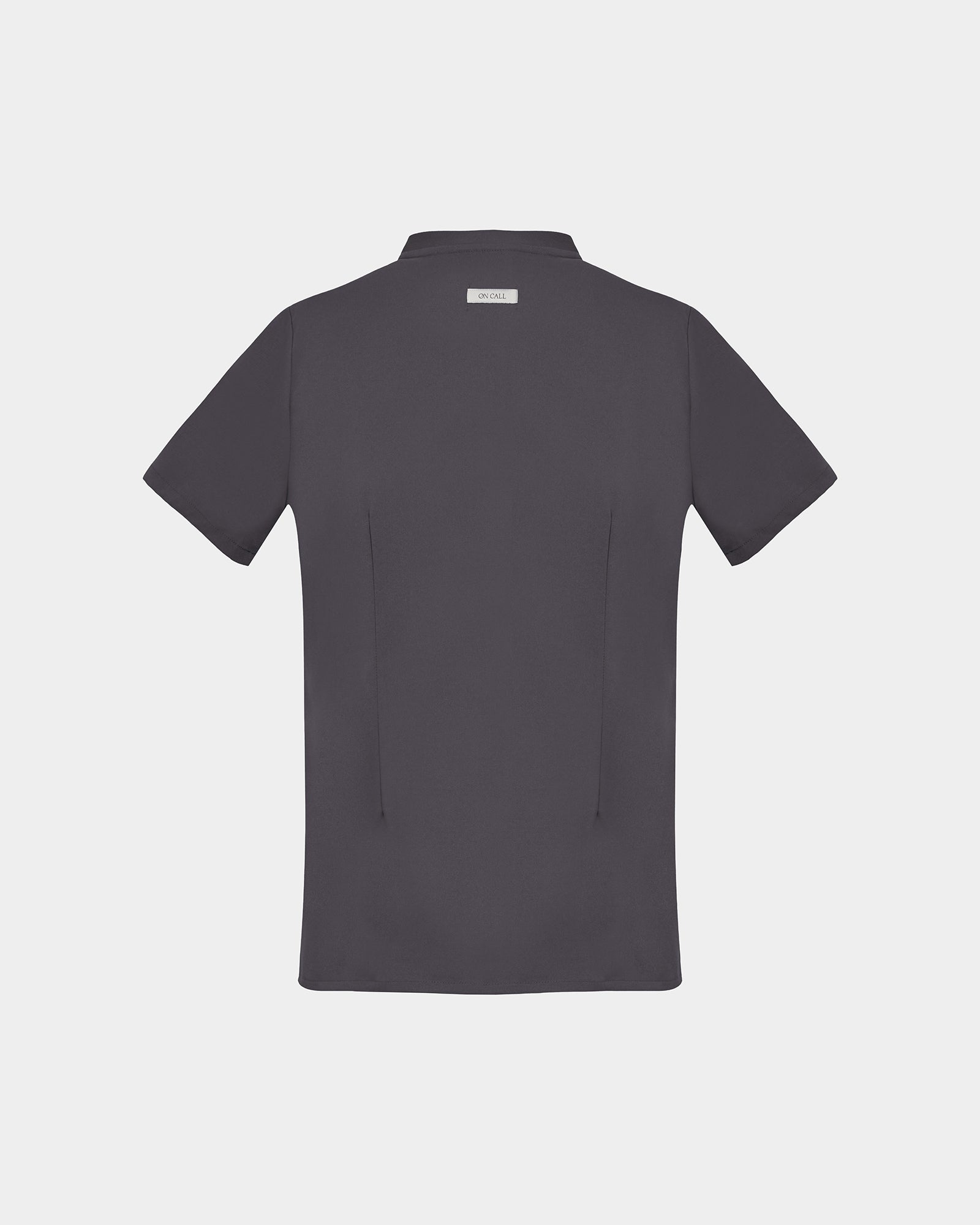 A dark grey short-sleeve scrub shirt shown from the back, featuring two back darts and a logo label, displayed on a light gray background.