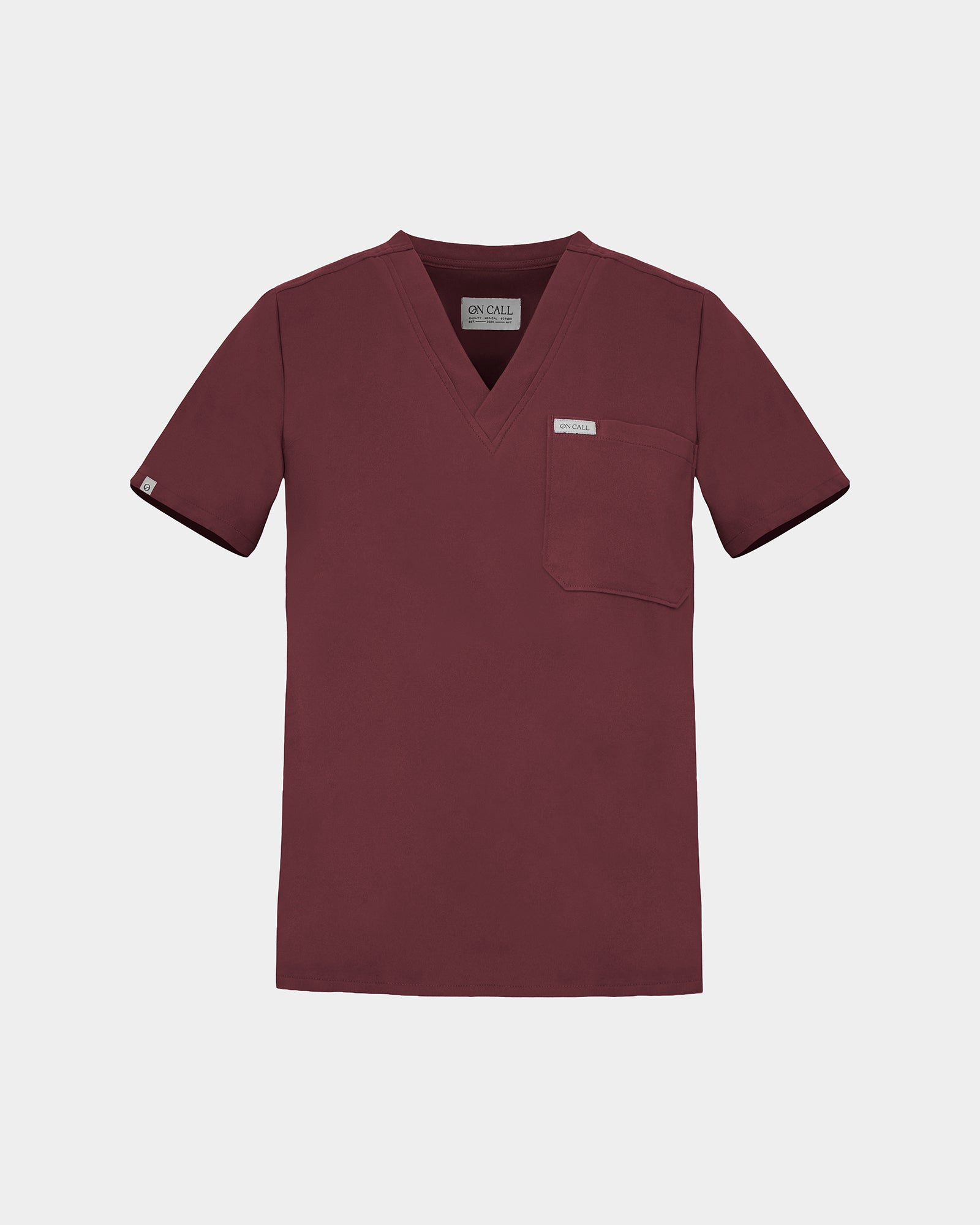 A short-sleeve V-neck scrub top in a deep heme red color with a chest pocket and a small white brand label, shown on a light gray background.