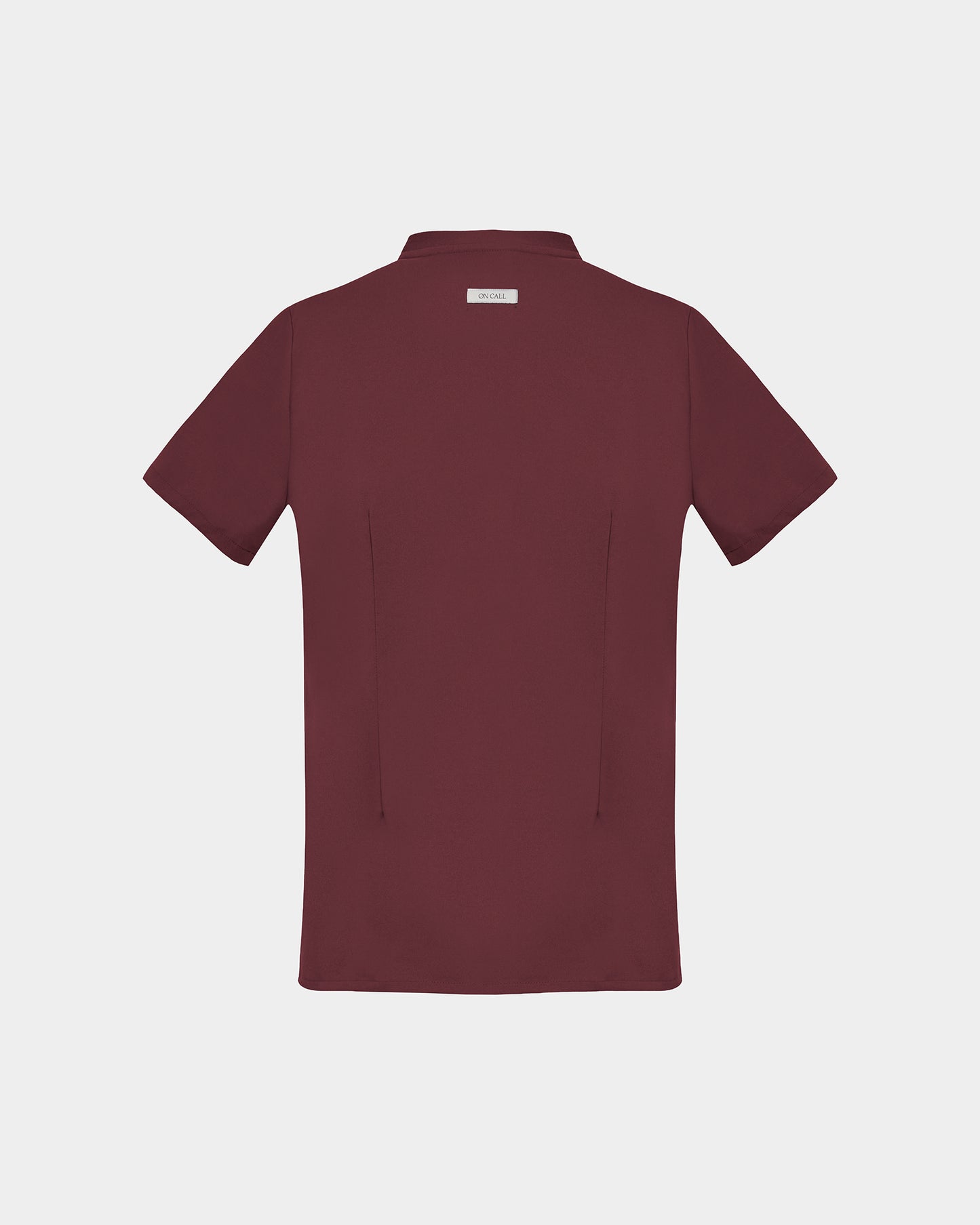 A short-sleeve scrub shirt in a deep heme red color, shown from the back, featuring two back darts, against a light gray background