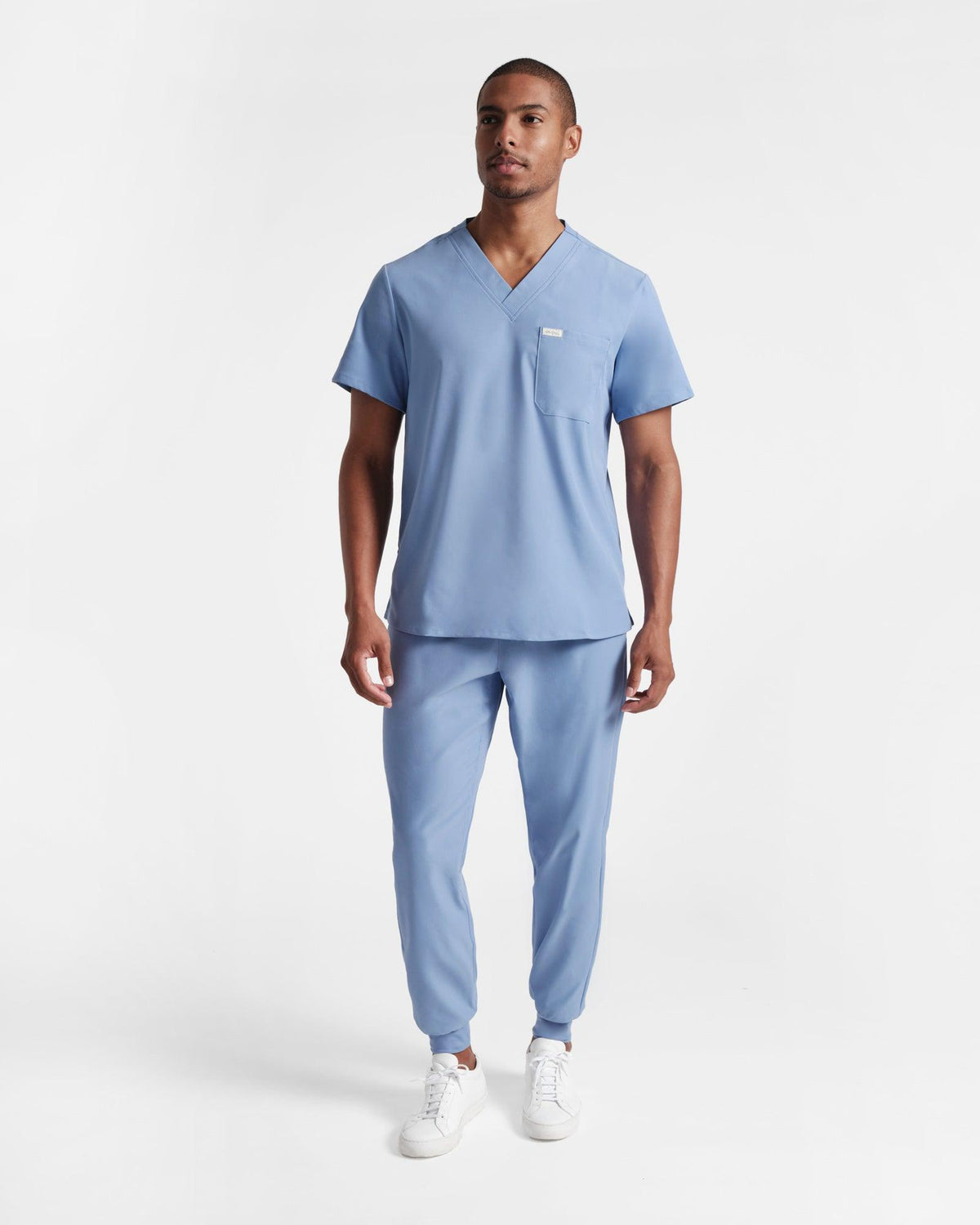 Man wearing a classic light blue scrub shirt untucked over jogger scrub pants.