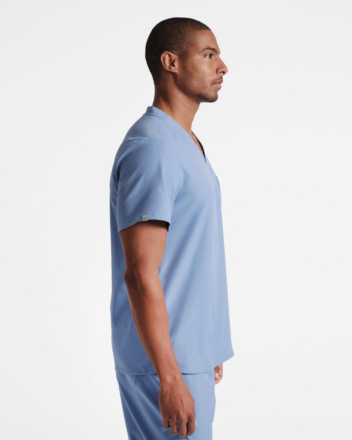 Side view of man wearing a light blue scrub shirt with a small logo fabric label wrapped around the sleeve's hem.