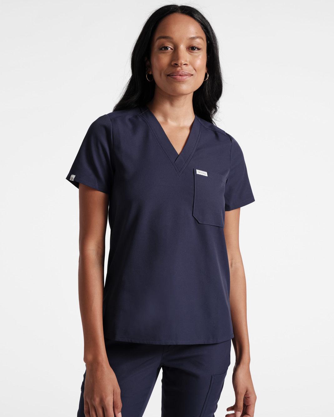 Woman in navy v-neck scrub shirt untucked over matching scrub pants.