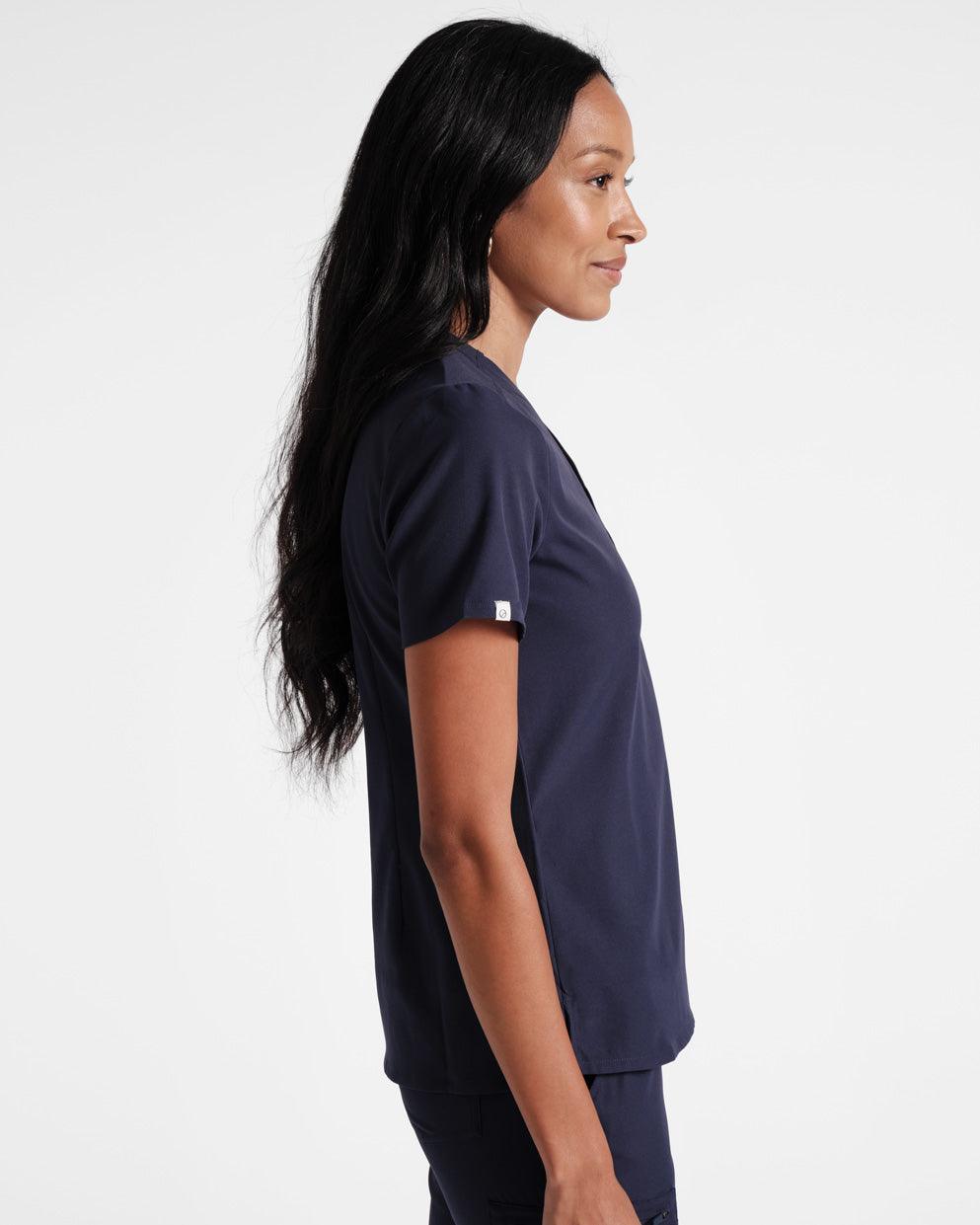 Side view of woman in navy scrub shirt with a small On Call fabric logo label wrapped around the sleeve hem. 