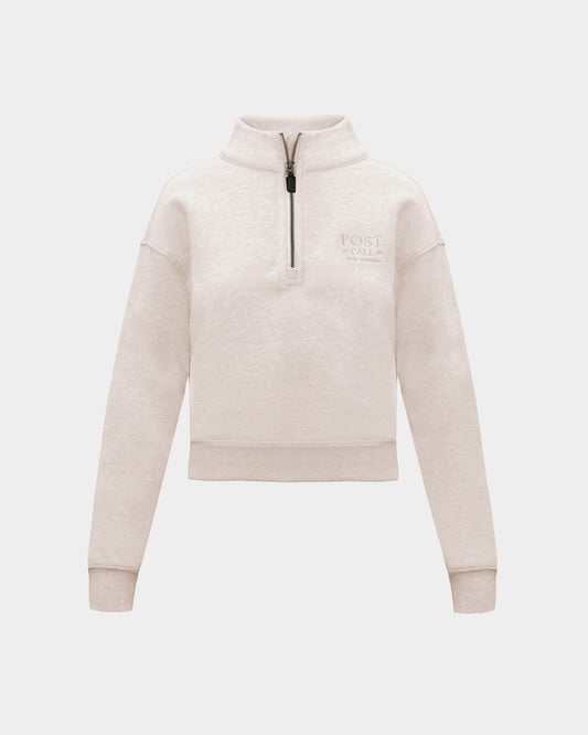 A heather beige half-zip sweatshirt with  small tonal embroidered logo on the left chest, displayed on a clean light gray background.