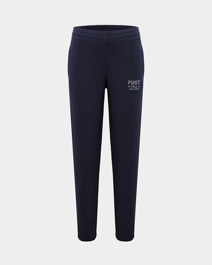 A pair of navy blue sweatpants with a white 'POST CALL' logo embroidered on the left thigh, shown against a light gray background.