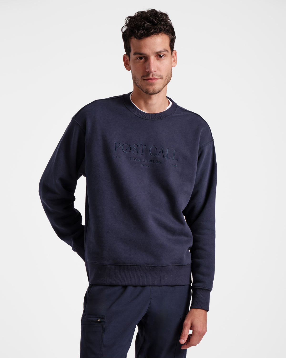 Man wearing unisex navy crewneck sweatshirt with tonal Post Call logo embroidery across the chest.