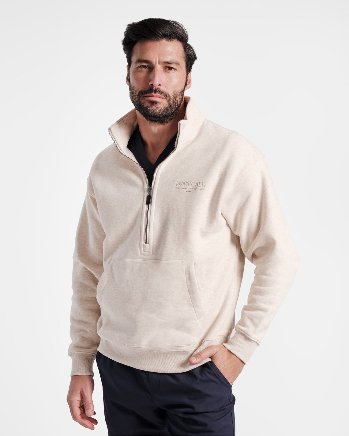 Man wearing heather beige half zip sweatshirt with a kangaroo pocket and tonal Post Call logo embroidered on the left chest.