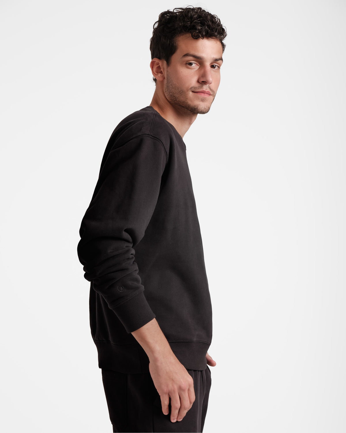 Side view of man wearing a black unisex crewneck sweatshirt with his sleeves pushed up.