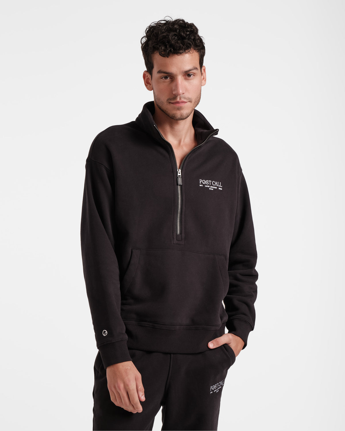 Man wearing black half zip sweatshirt with a kangaroo pocket and white Post Call logo embroidered on the left chest.