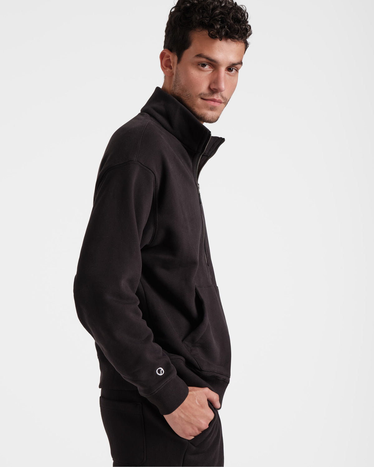 Side view of man wearing black half zip sweatshirt with a kangaroo pocket and white Post Call emblem logo above the wrist cuff.