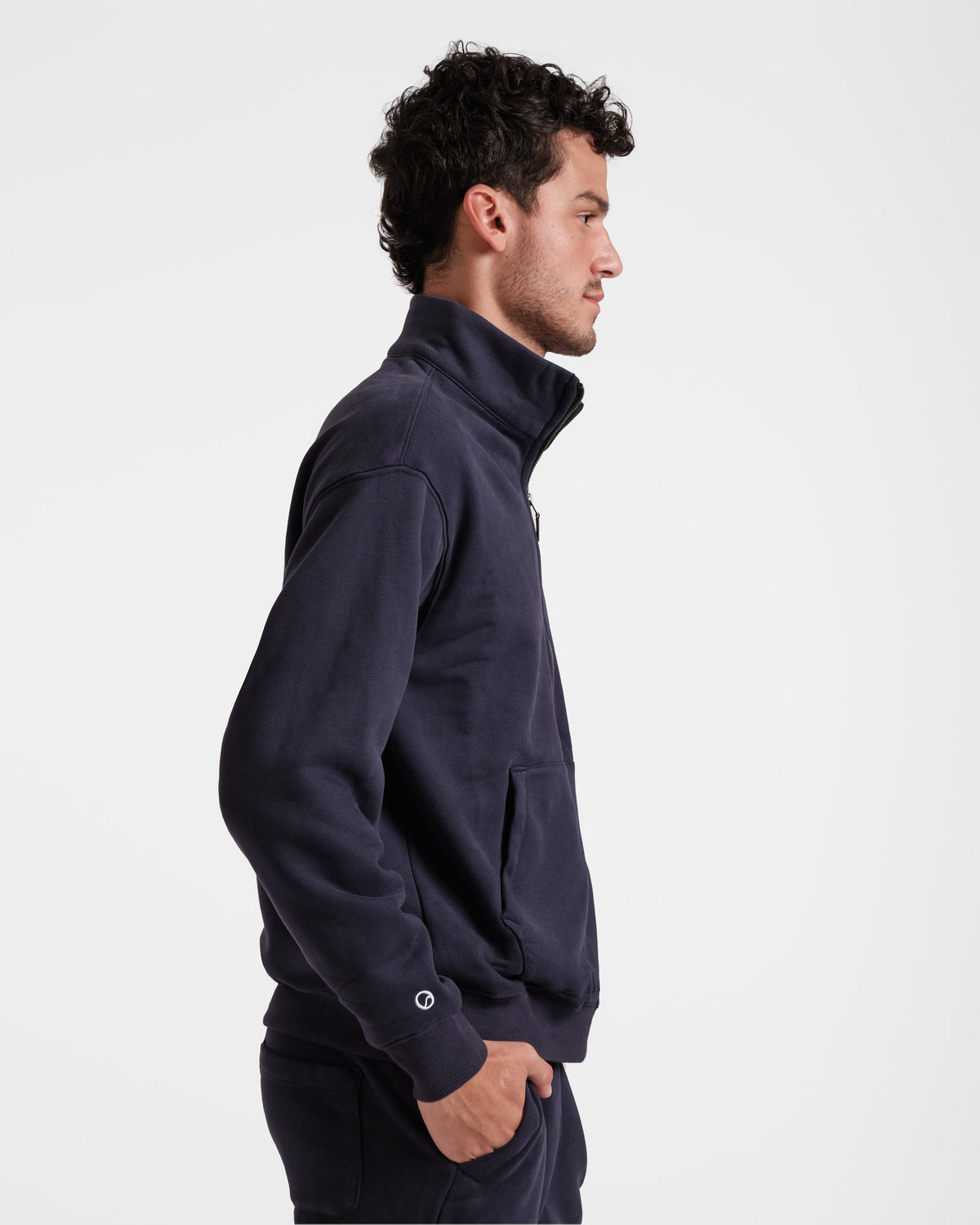 Side view of man wearing navy half zip sweatshirt with white Post Call emblem logo above wrist cuff. 