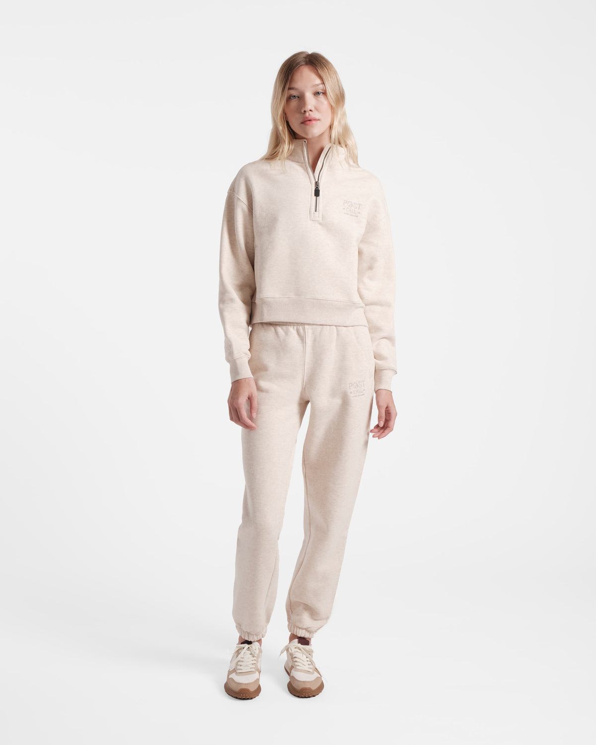 Woman wearing a heather beige half zip sweatshirt with matching jogger sweatpants.