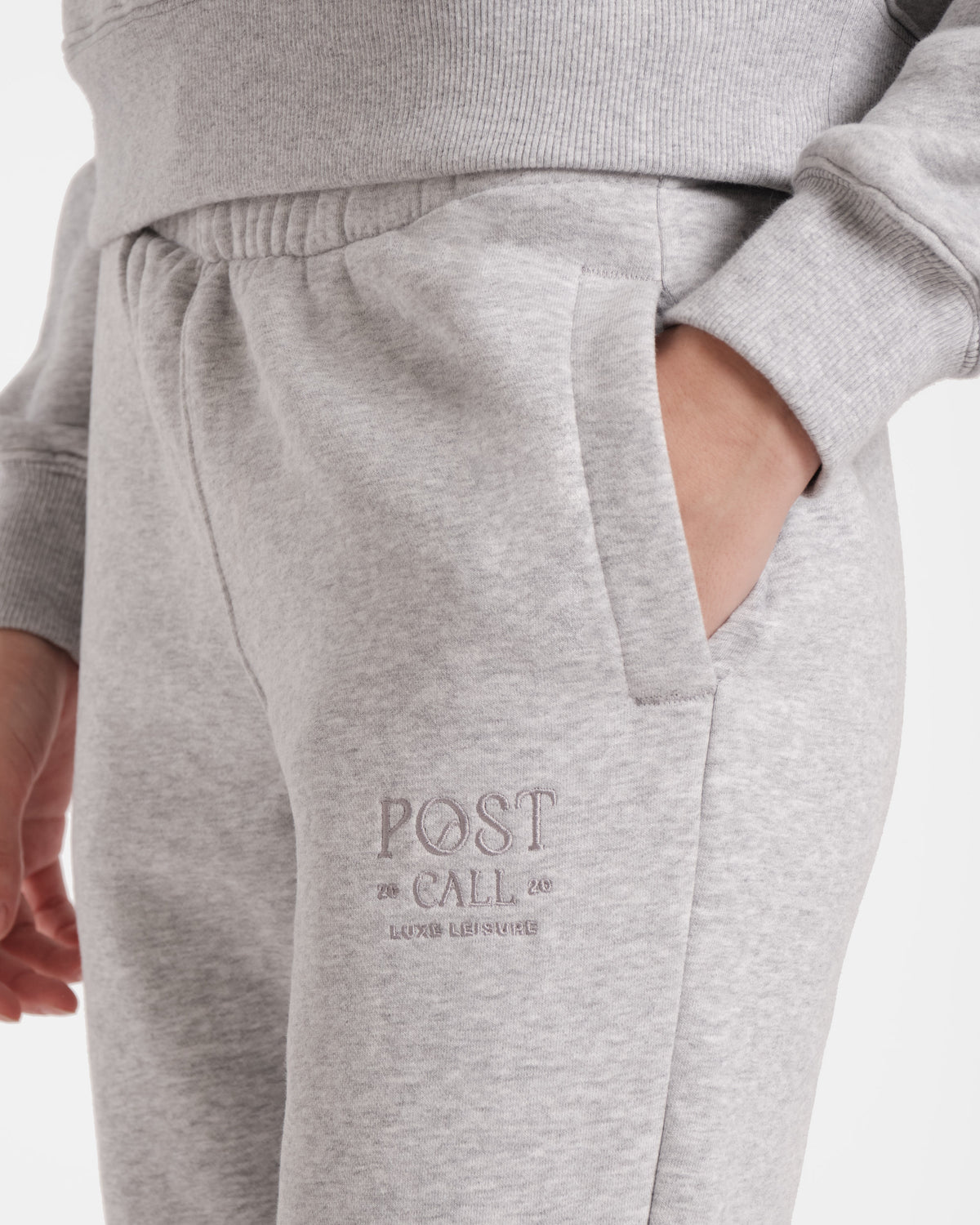 Close up view of model's hand in the side pocket with tonal logo Post Call embroidery on the upper thigh, all in heather grey.