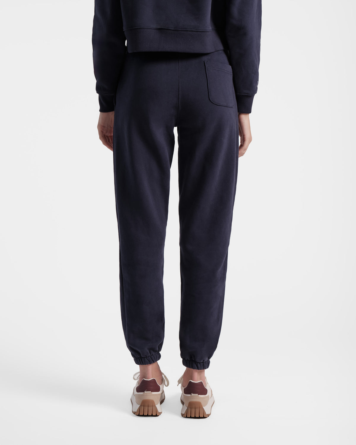 Back side view of woman wearing navy jogger sweatpants with elasticated ankle cuffs and one back pocket. 