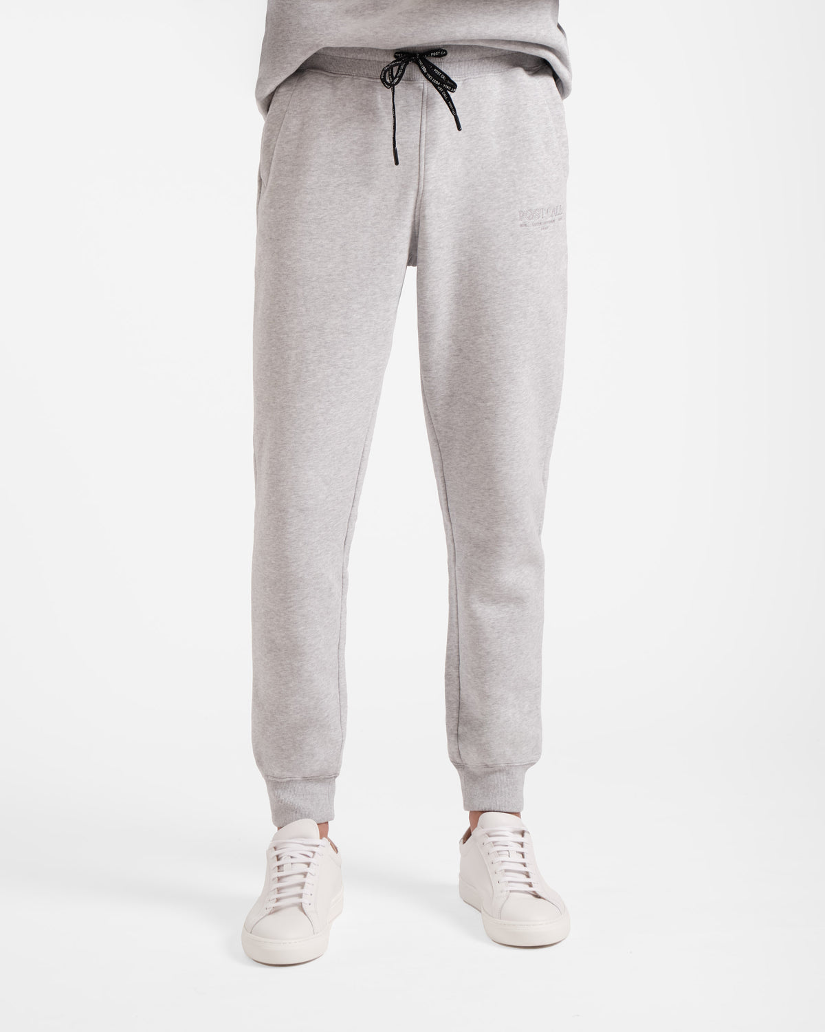 Waist down view of man wearing heather grey jogger sweatpants with stretch ankle cuffs and black contrast branded waist tie.